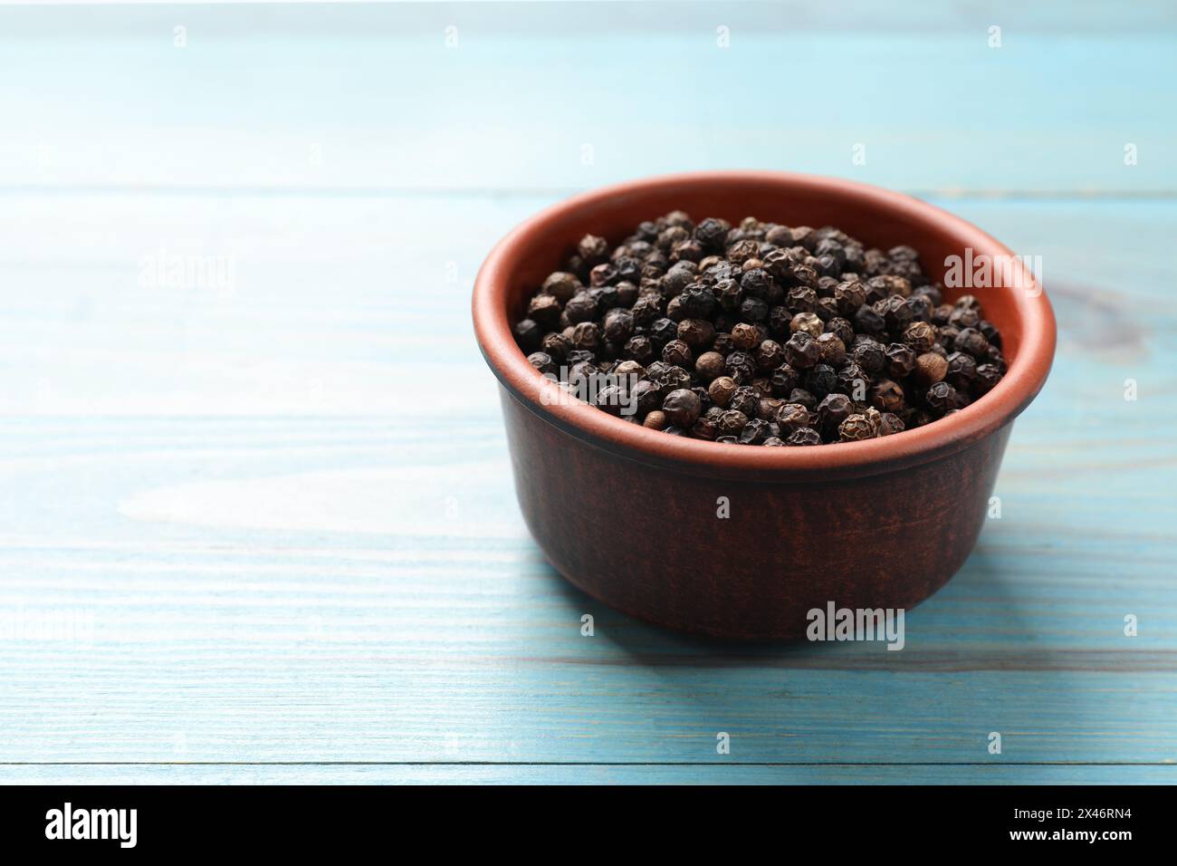 Aromatisches Gewürz. Schwarzer Pfeffer in Schüssel auf hellblauem Holztisch, Platz für Text Stockfoto