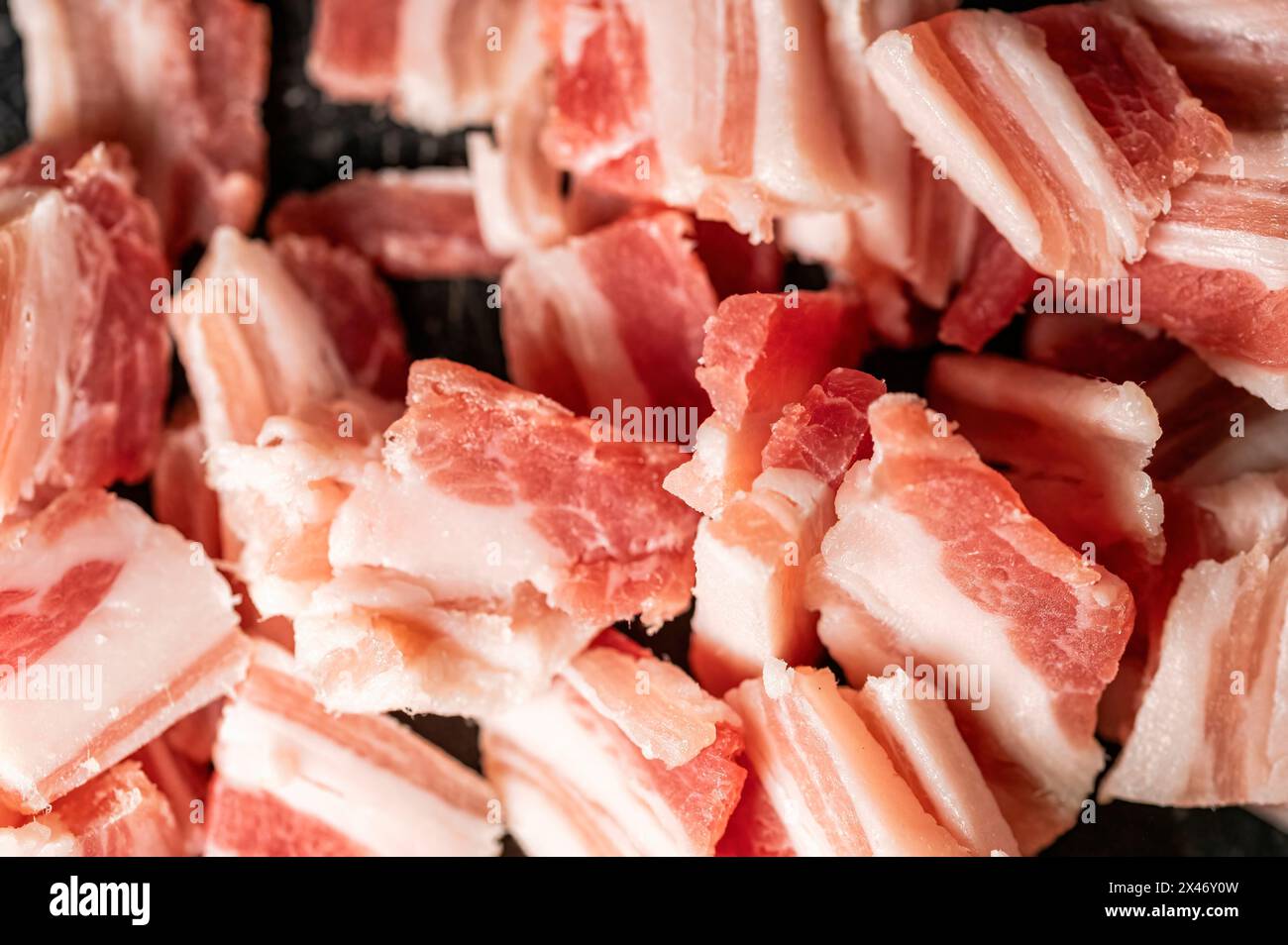 Schweinebauchstücke, die in Stücke geschnitten werden, um ein Gericht wie Spaghetti Carbonara zu kochen und einen Hintergrund zu schaffen Stockfoto