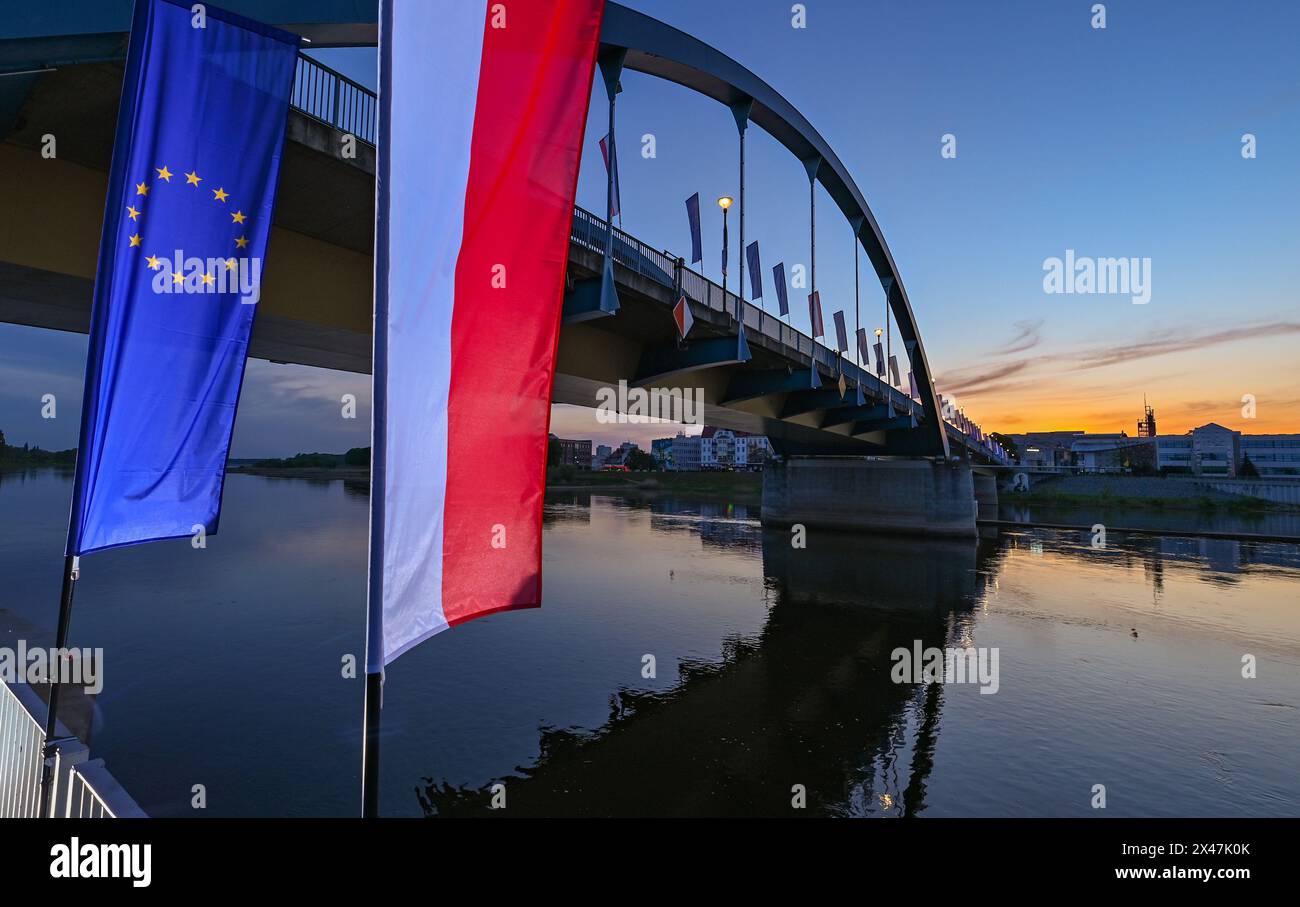 01. Mai 2024, Brandenburg, Frankfurt (oder): Die Flagge der Europäischen Union und die Nationalflagge Polens winken bei Sonnenaufgang im Wind vor der Stadtbrücke über die oder zwischen Frankfurt (oder) und Slubice in Polen. Am 20. Jahrestag des EU-Beitritts Polens planen die Außenminister der beiden Nachbarländer, sich mittags zu treffen. Beide wollen das Collegium Polonicum in Slubice auf polnischer Seite besuchen, sowie ein europäisches Festival, und dann gemeinsam über die Stadtbrücke über die deutsch-polnische Grenze oder nach Frankfurt (oder) laufen. Foto: Patrick Stockfoto