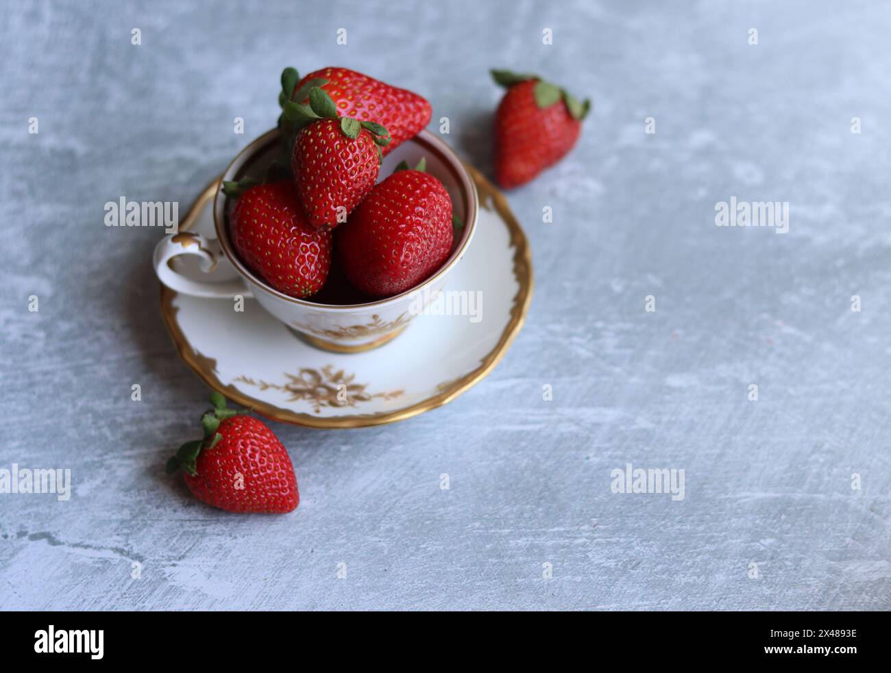 Erdbeeren in weißer Porzellanschale im Retro-Stil vor hellgrauem, strukturiertem Hintergrund mit Platz für Text. Sommersaison Bio-Obst. Frisches Essen. Stockfoto
