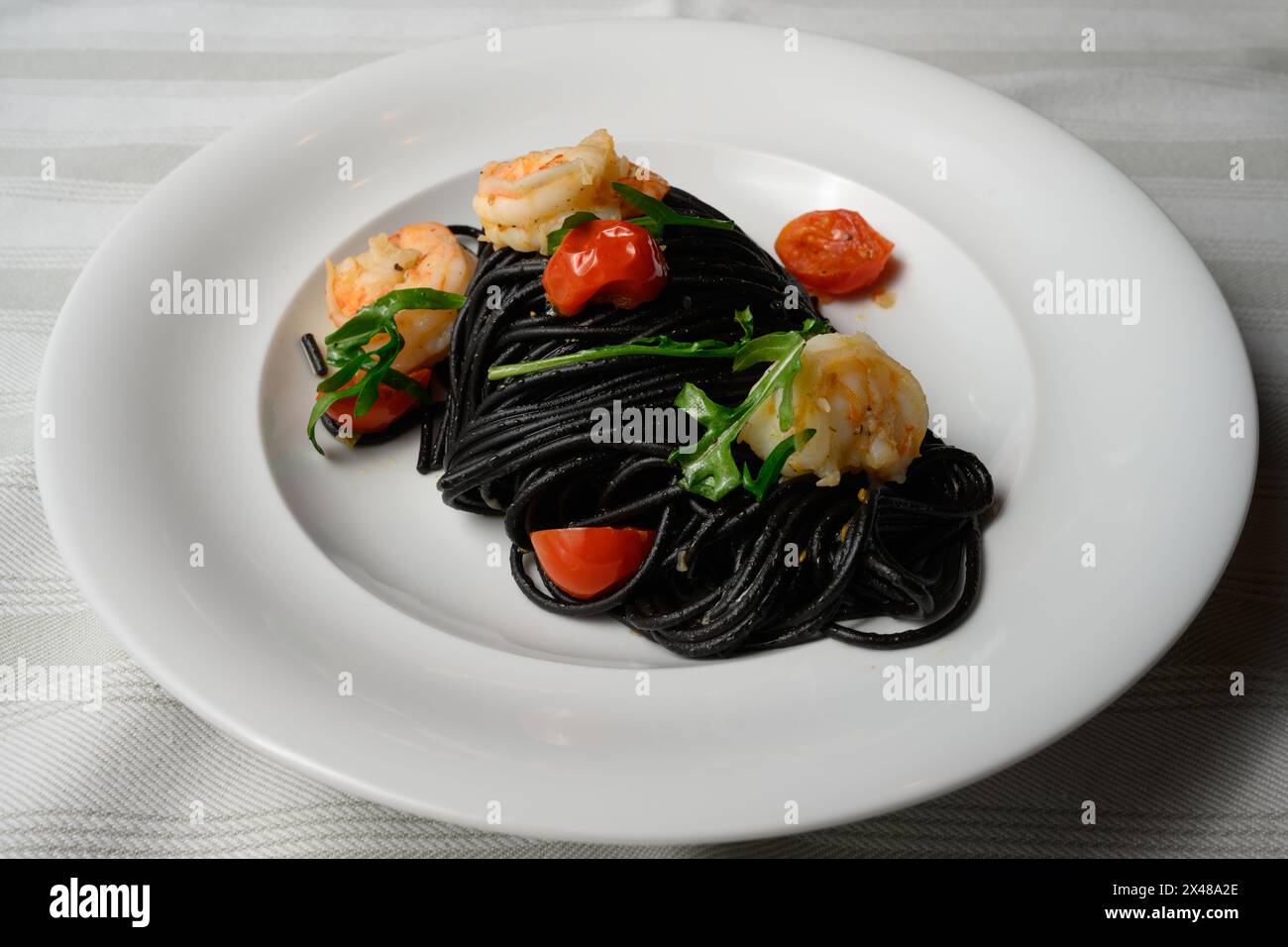 Spaghetti al Nero di Seppia con Gamberi, italienische Pasta mit Tintenfischtinte, Garnelen, Tomaten und Rucola Stockfoto