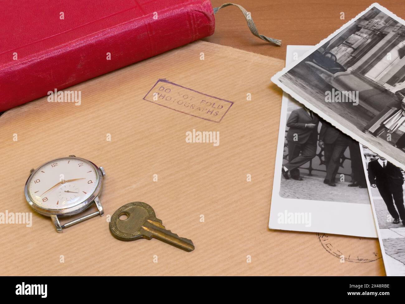 Schreibtisch mit einem Umschlag für Fotos, ein paar alte Fotos, ein Schlüssel, eine Vintage-Uhr und ein Buch mit rotem Einband Stockfoto