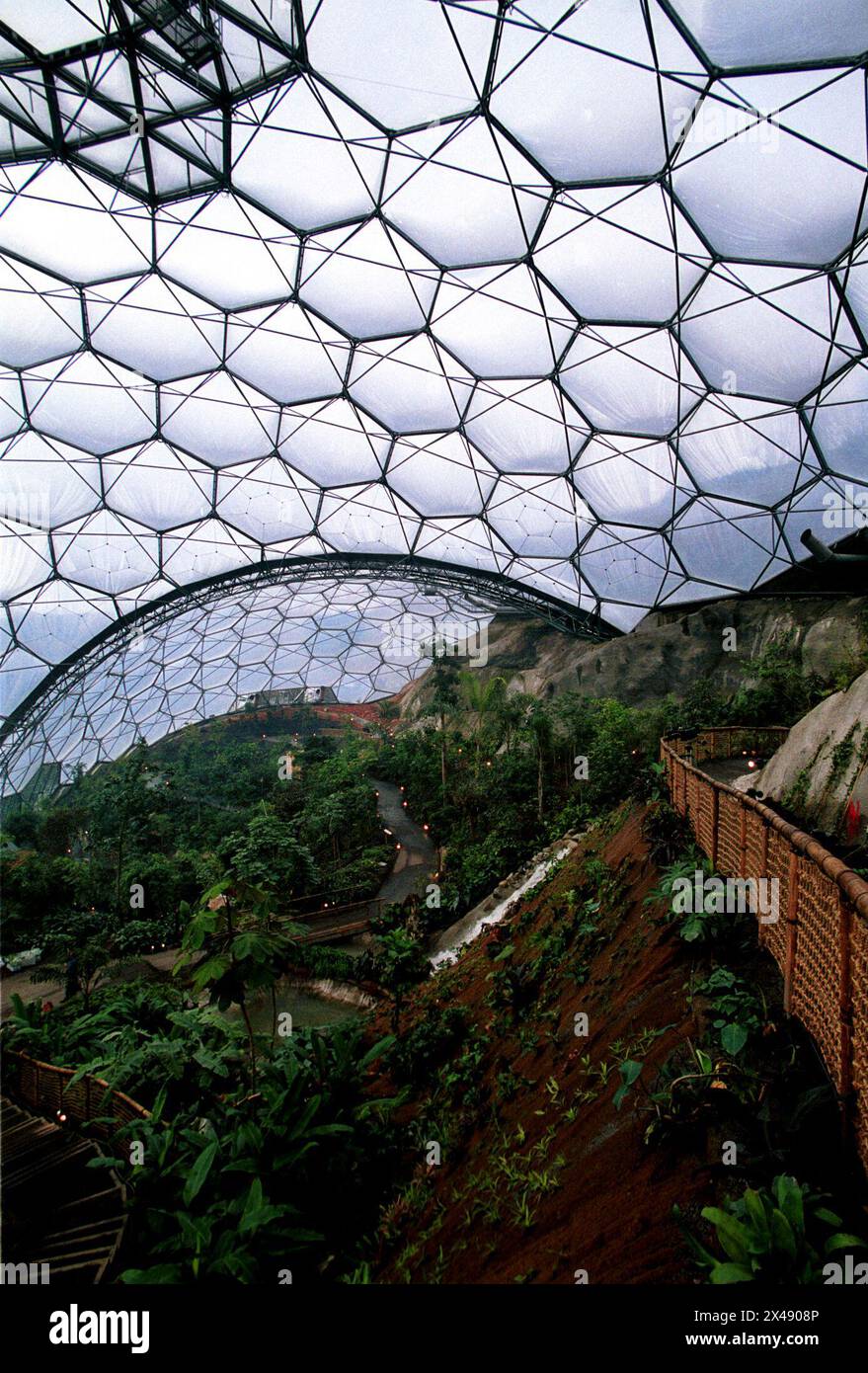 Eden Project Cornwall Mai 2001 das Eden Project (Cornish: Edenva) ist eine Besucherattraktion in Cornwall, England. Das Projekt befindet sich in einer zurückgewonnenen china-Tongrube, 2 km (1,2 mi) von der Stadt St Blazey und 5 km (3 mi) entfernt. der Komplex wird von zwei riesigen Gehegen dominiert, die aus benachbarten Kuppeln bestehen, die Tausende von Pflanzenarten beherbergen.[3] jedes Gehege emuliert ein natürliches Biom. Die Biome bestehen aus Hunderten sechseckiger und fünfeckiger Ethylentetrafluorethylen (ETFE)-Zellen, die von geodätischen Stahlrohrkuppeln unterstützt werden. Je größer Stockfoto