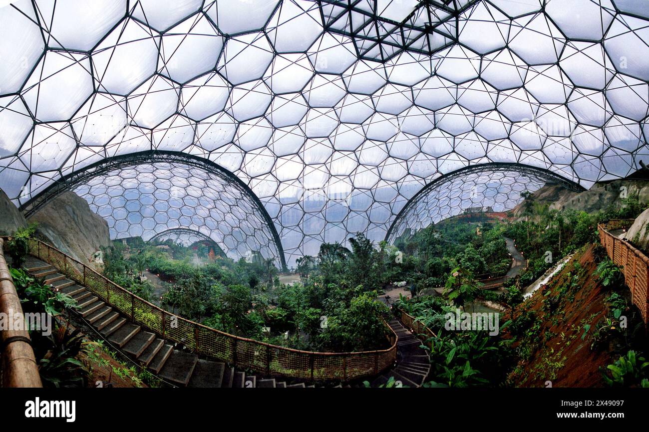 Eden Project Cornwall Mai 2001 das Eden Project (Cornish: Edenva) ist eine Besucherattraktion in Cornwall, England. Das Projekt befindet sich in einer zurückgewonnenen china-Tongrube, 2 km (1,2 mi) von der Stadt St Blazey und 5 km (3 mi) entfernt. der Komplex wird von zwei riesigen Gehegen dominiert, die aus benachbarten Kuppeln bestehen, die Tausende von Pflanzenarten beherbergen.[3] jedes Gehege emuliert ein natürliches Biom. Die Biome bestehen aus Hunderten sechseckiger und fünfeckiger Ethylentetrafluorethylen (ETFE)-Zellen, die von geodätischen Stahlrohrkuppeln unterstützt werden. Je größer Stockfoto