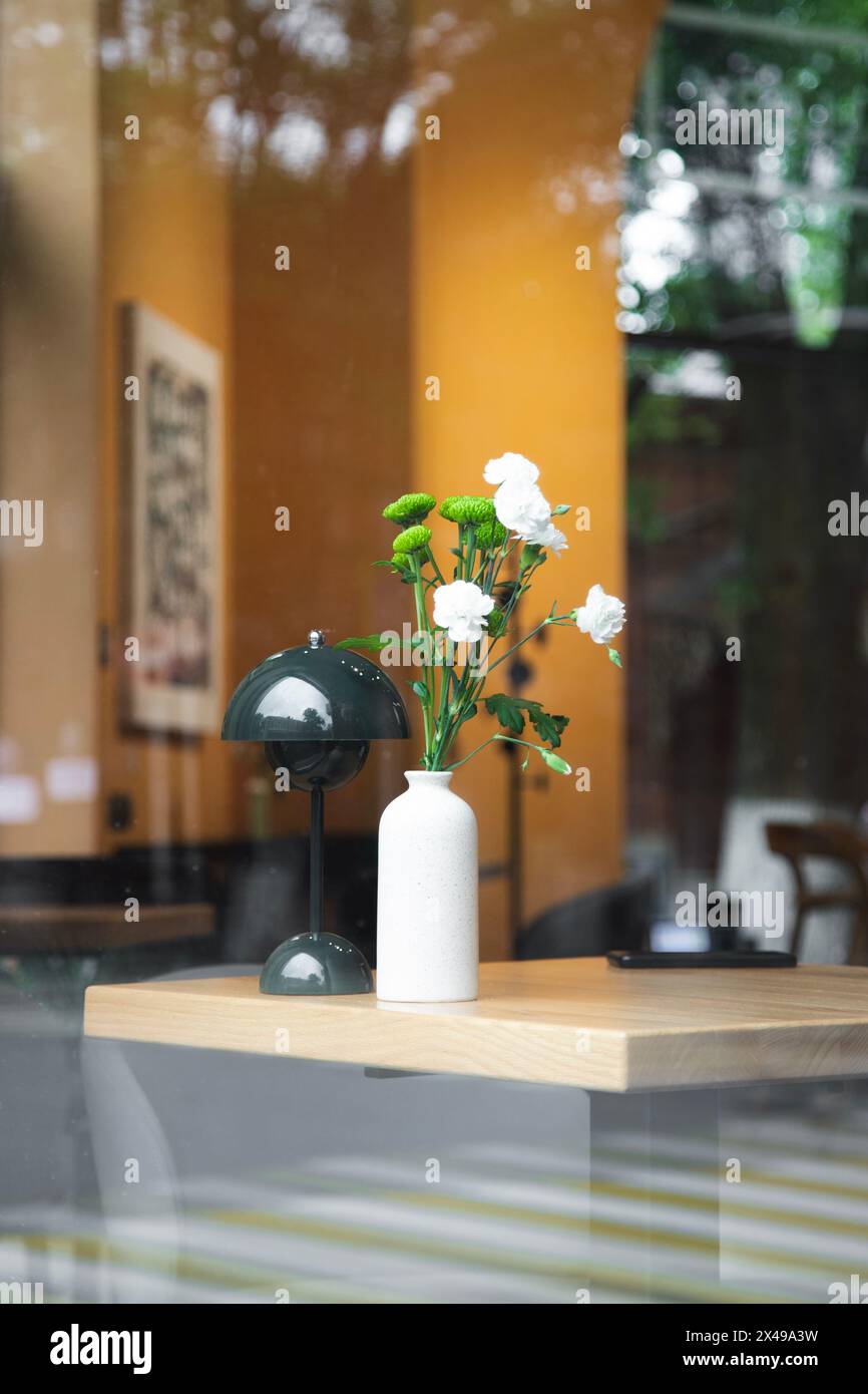 Von außen durch das Fenster geschossen. Blumen- und Schreibtischlampe auf dem Tisch im gemütlichen Café. Stilvolles, modisches, modernes Design eines Cafés Stockfoto