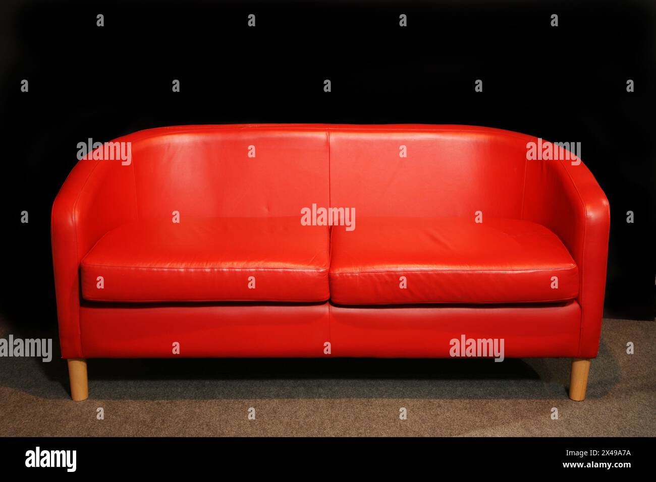 Rotes Sofa im Retro-Stil der 60er Jahre vor dunkler Wand Stockfoto