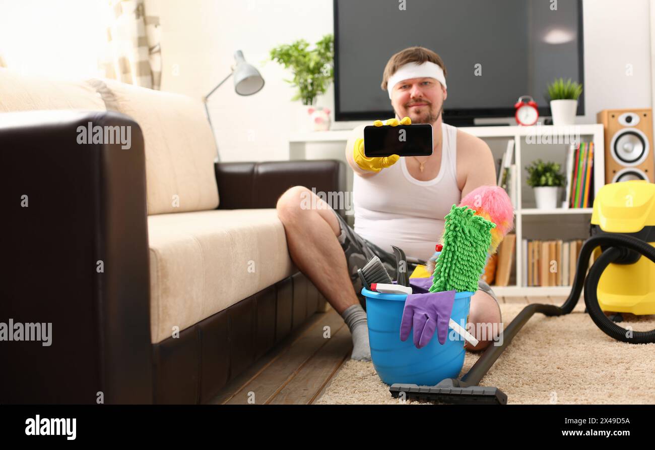 Eine junge lächelnde Mann hält ein Smartphone in seiner Hand es demonstrieren, um die Kamera Werbung eine mobile Anwendung für die Reinigung zu suchen Stockfoto