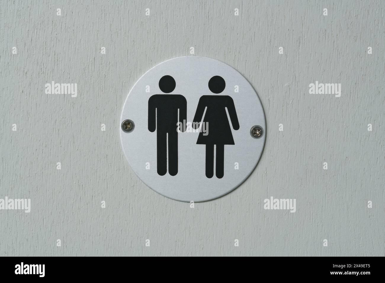 Toilettenzeichen an einer Tür. Ein Symbol für die Toilette aus gebürstetem Aluminium, das an eine Tür geschraubt ist. Beide Geschlechter. Gemischt. Stockfoto