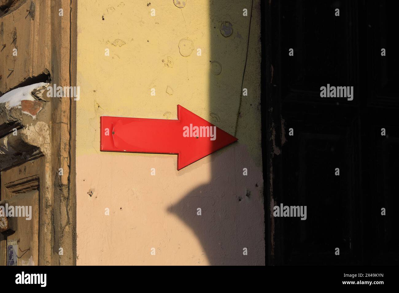 An der gelben Wand des Hauses befindet sich ein roter Pfeil rechts im Schatten Stockfoto