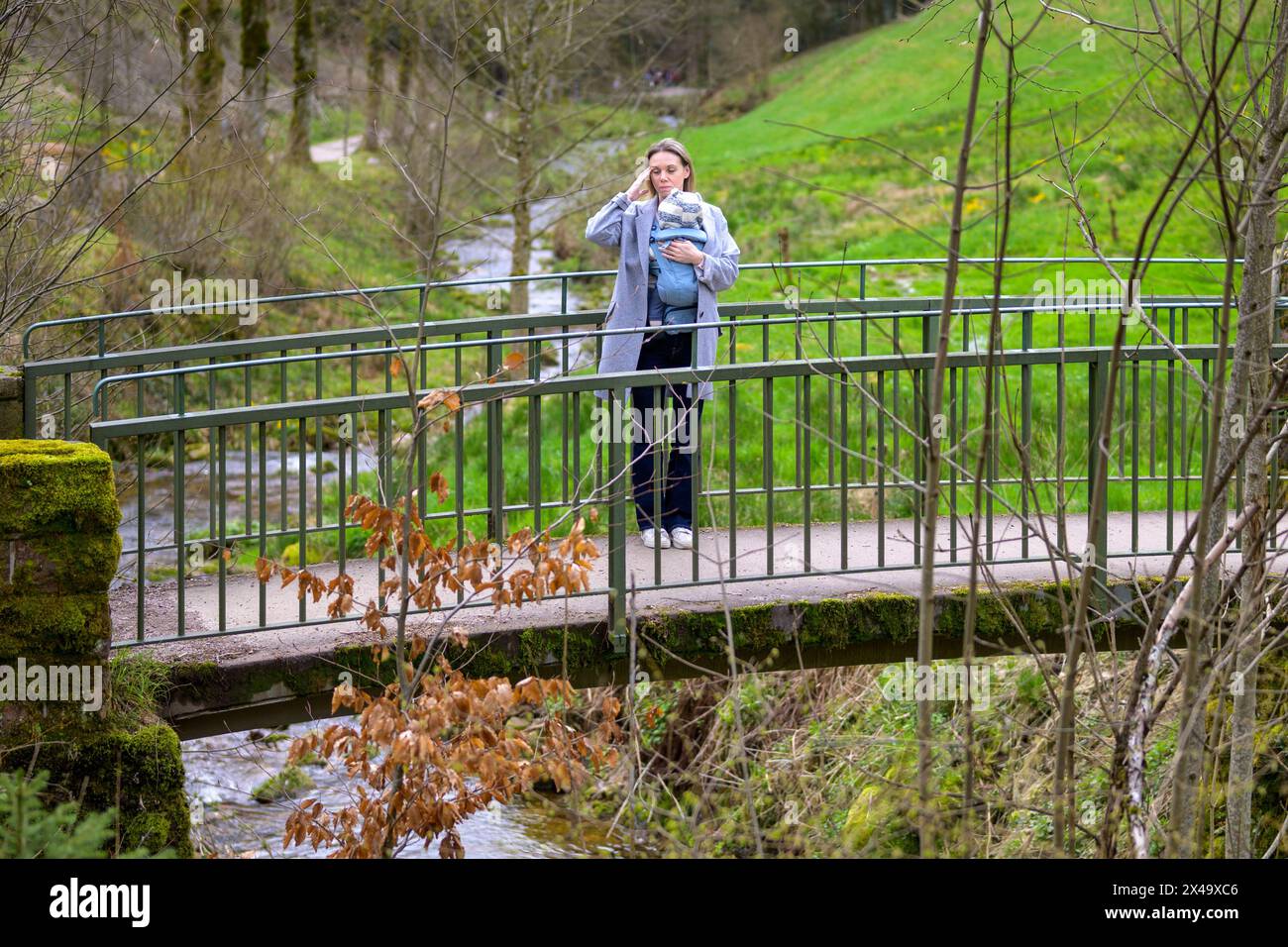 Gestresste, erschöpfte und depressive Frau, die mit ihrem kleinen Baby auf einer Brücke in der Natur steht Stockfoto