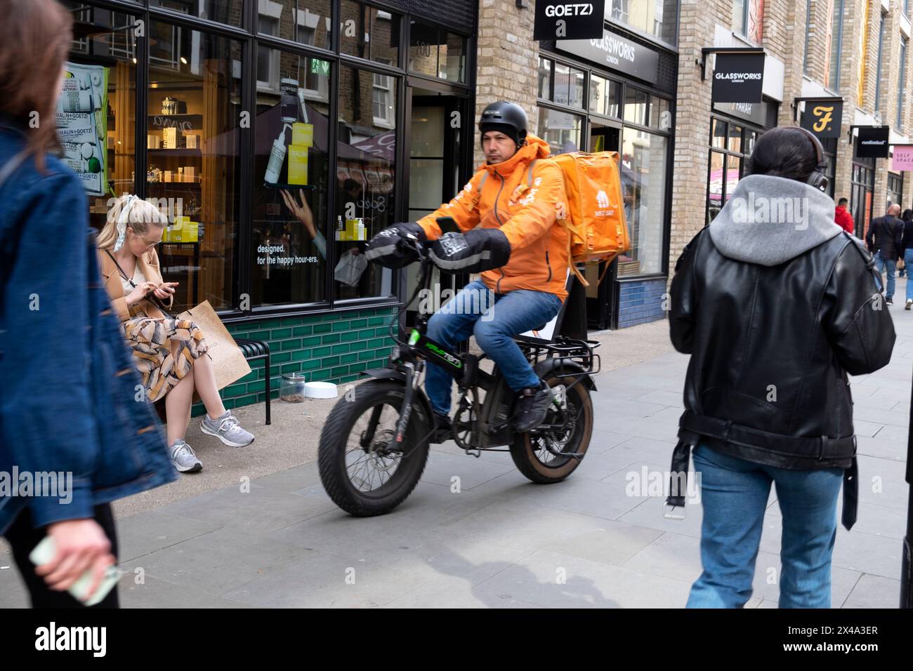 Essen Sie einfach Essen Lieferung Kurier Radfahrer Fahrrad fahren Fahrrad auf Gehsteig vor kleinen Geschäften in Berwick Street London England Großbritannien 2024 KATHY DEWITT Stockfoto