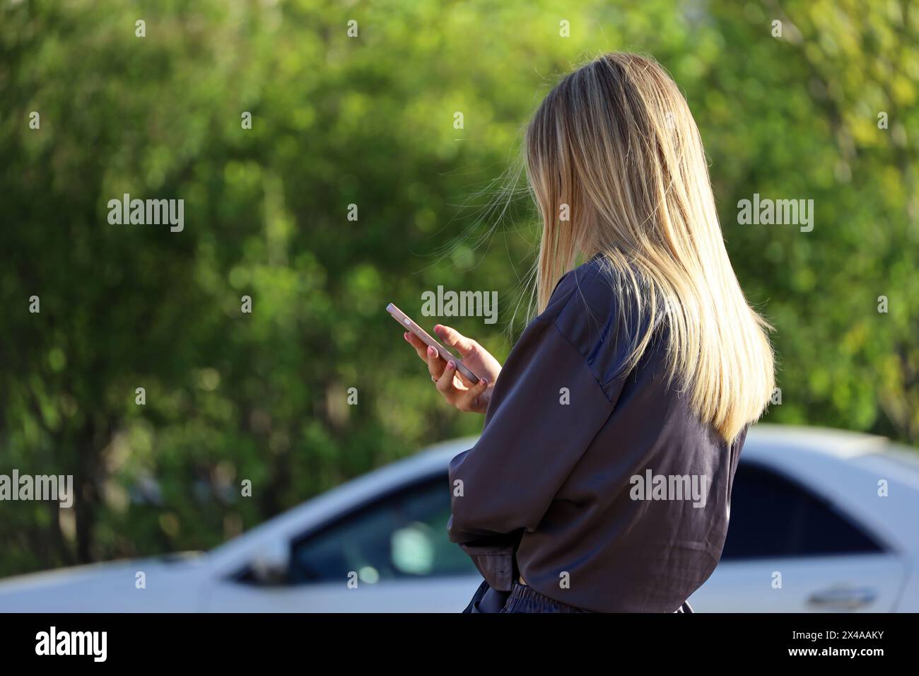 Mädchen mit langen blonden Haaren mit Smartphone auf der Stadtstraße auf verschwommenem Autohintergrund Stockfoto
