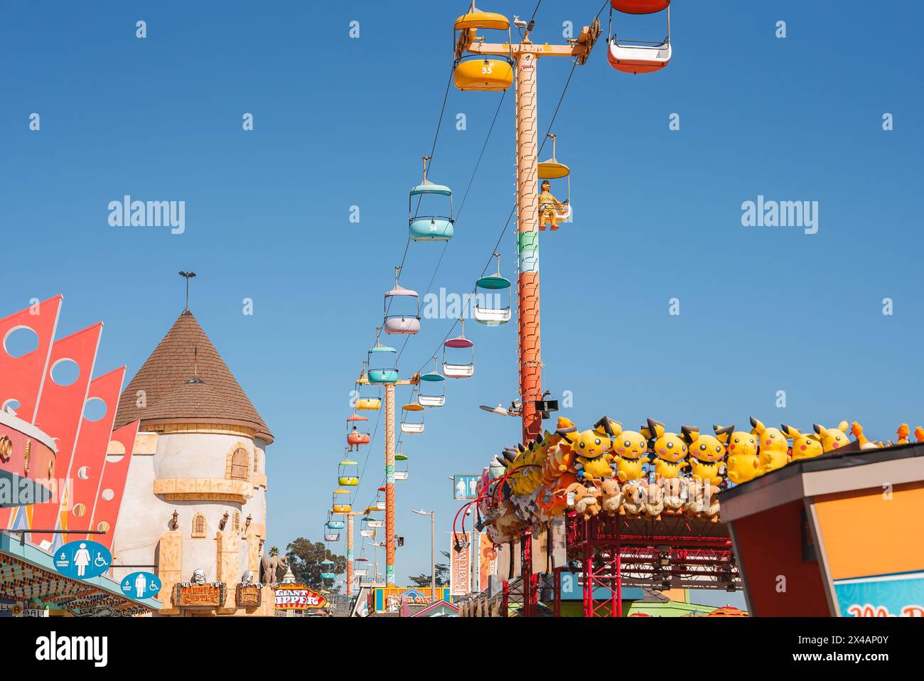 Farbenfrohe Vergnügungspark-Szene mit Pikachu-Preisen und Sky-Ride-Attraktion bei sonnigem Wetter. Stockfoto