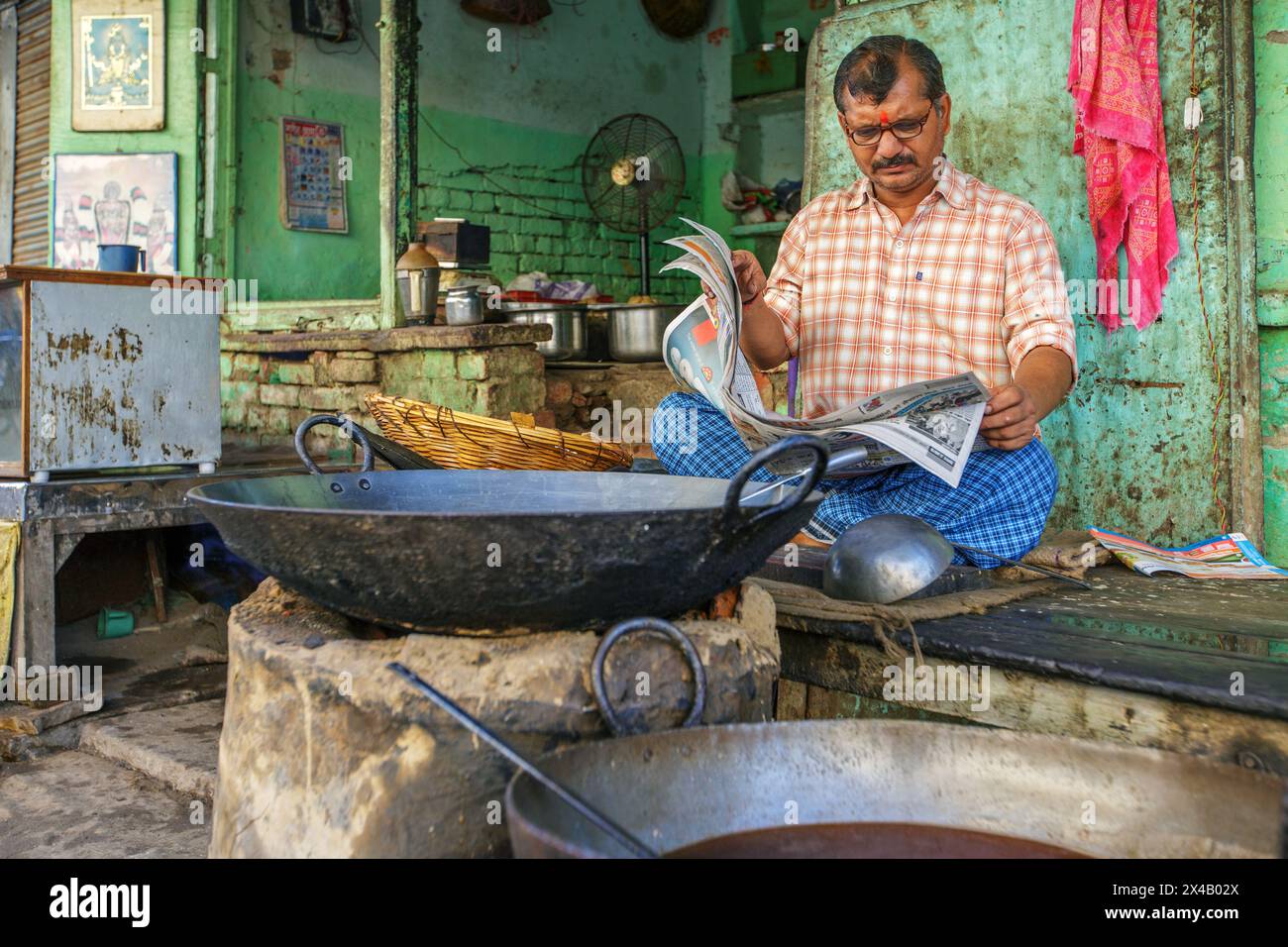 Der Besitzer eines Lebensmittelgeschäfts liest eine Zeitung in Varanasi, Indien. Stockfoto