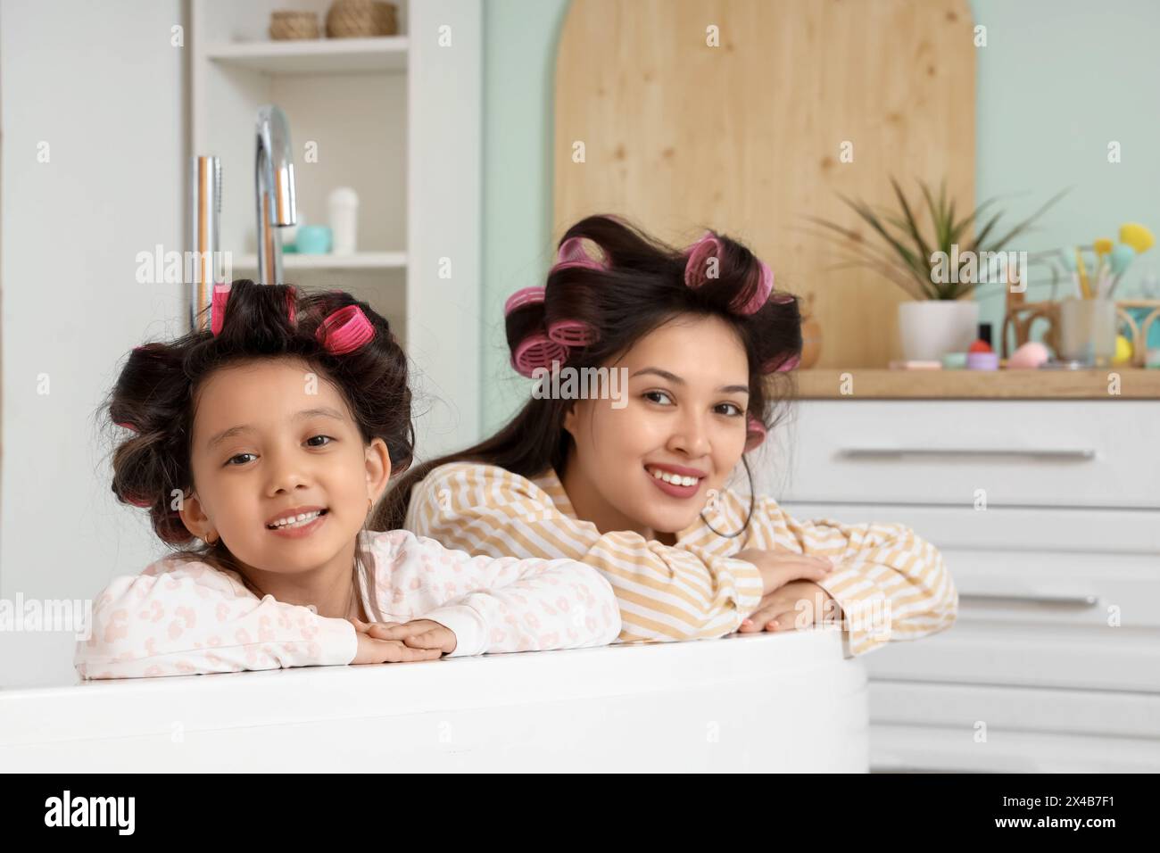 Das kleine asiatische Mädchen und ihre Mutter mit Lockenwicklern in der Badewanne zu Hause Stockfoto
