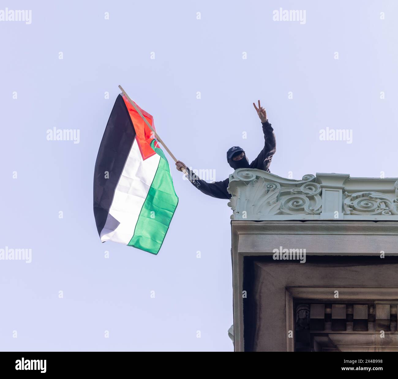 NEW YORK, New YORK – 30. April 2024: Ein Demonstrant schwingt eine palästinensische Flagge auf dem Dach der Hamilton Hall an der Columbia University in Manhattan. Stockfoto