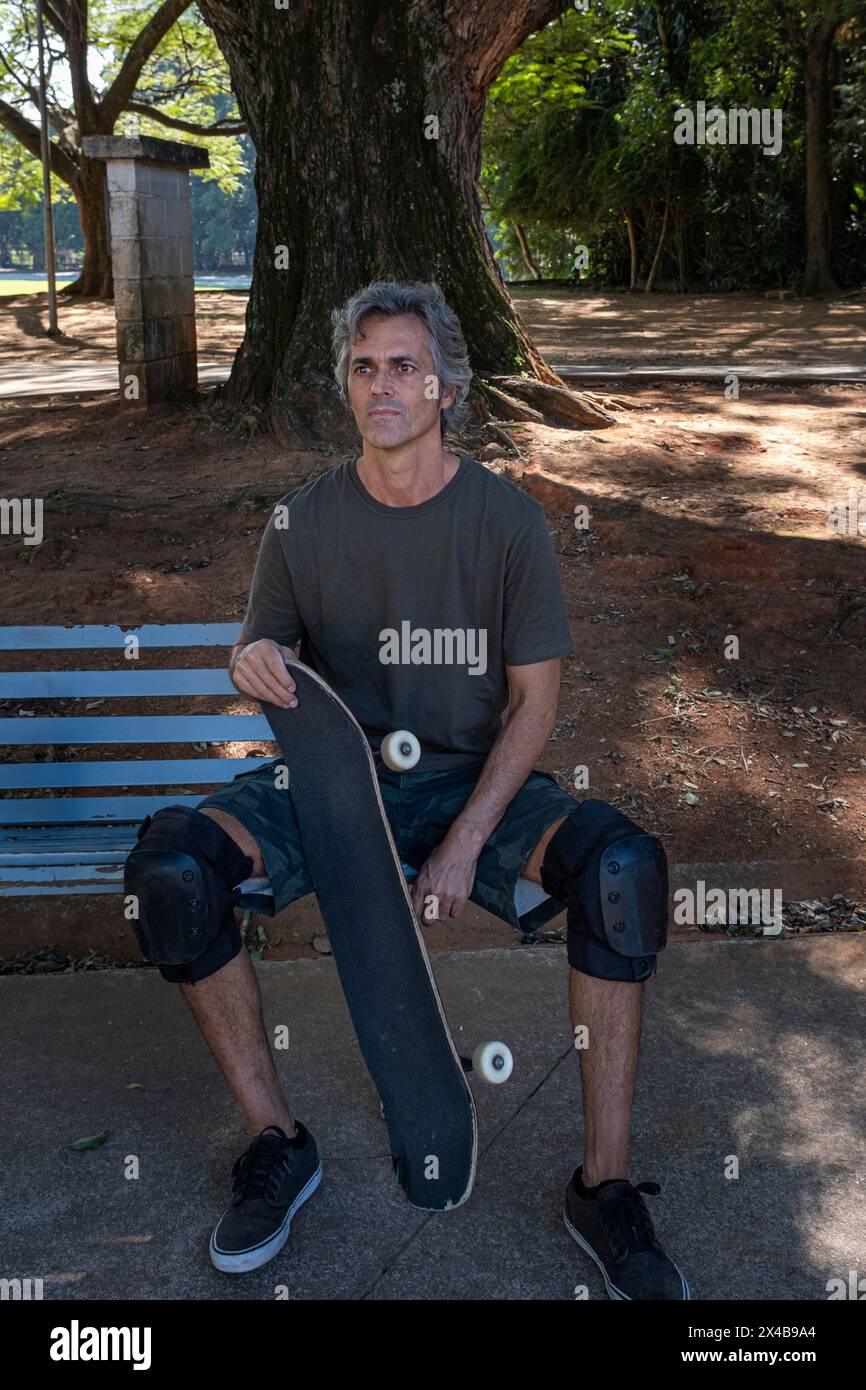 Brasilianischer Skateboarder, der über 50 Jahre alt ist und sich auf einer Bank in einem Quadrat entspannt 2. Stockfoto