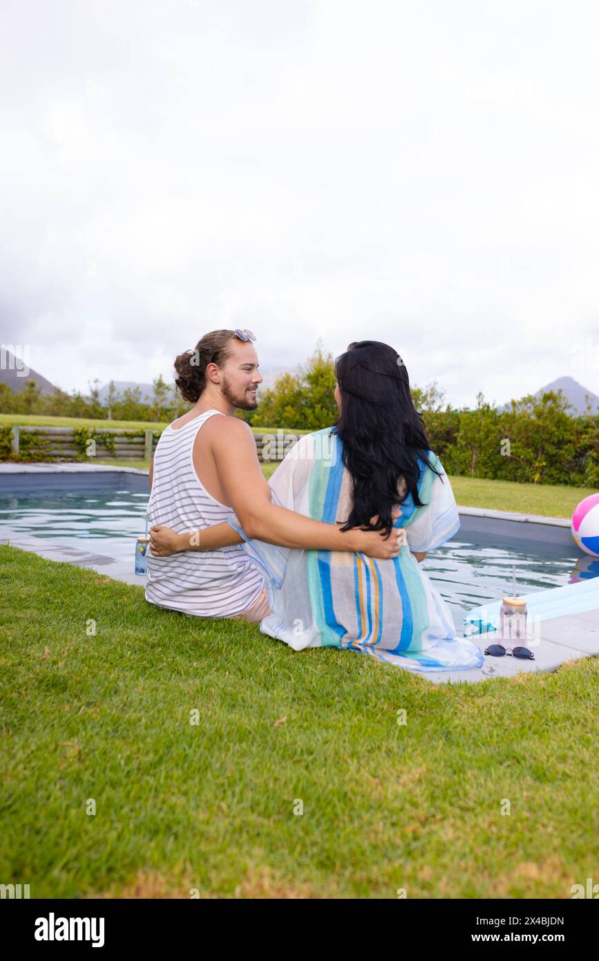 Verschiedene Paare genießen die Gesellschaft des anderen im Freien am Pool, Kopierraum. Sie, mit langen schwarzen Haaren, und er, mit Bart und lockigem Haar, ist entspannt Stockfoto