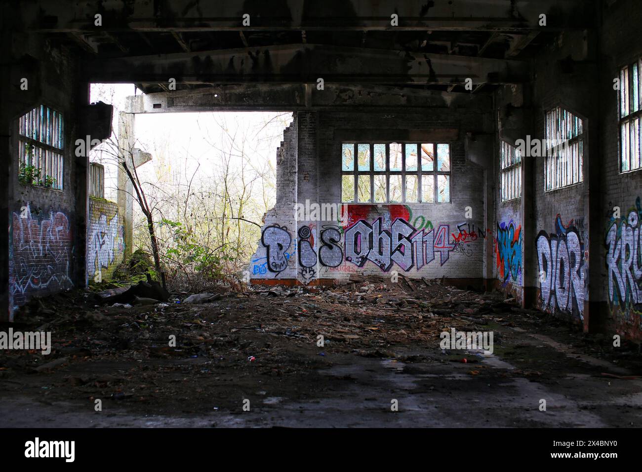 Teilweise eingestürzte Fabrikhalle mit Graffiti, gefüllt mit Trümmern. Stockfoto