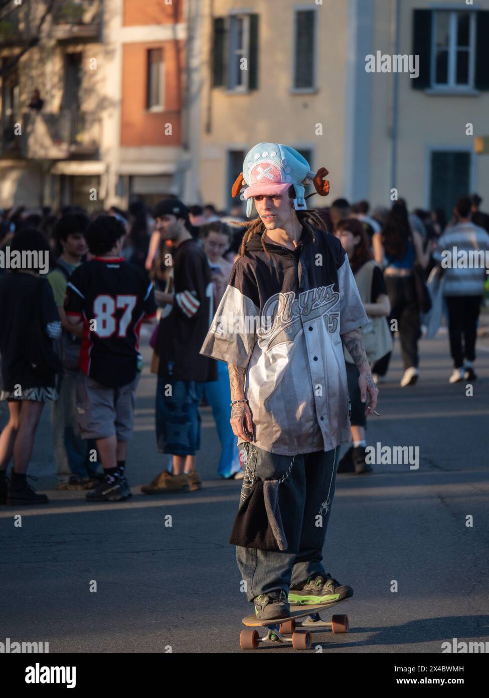 Junge mit lustigem Hut und Rasta-Haar und Joint spielt mit seinem Skateboard während einer Street Rave Party. Stockfoto