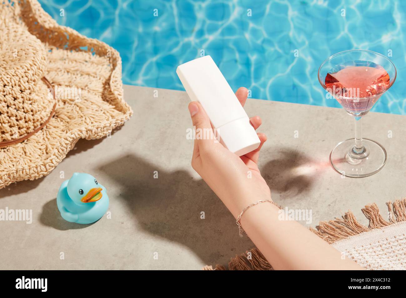 Sommerurlaub mit Swimmingpool und klarem blauem Wasser, dekorierten Hüten und Weingläsern. Die Hand der Frau hält eine Tube Sonnencreme ohne Labe Stockfoto