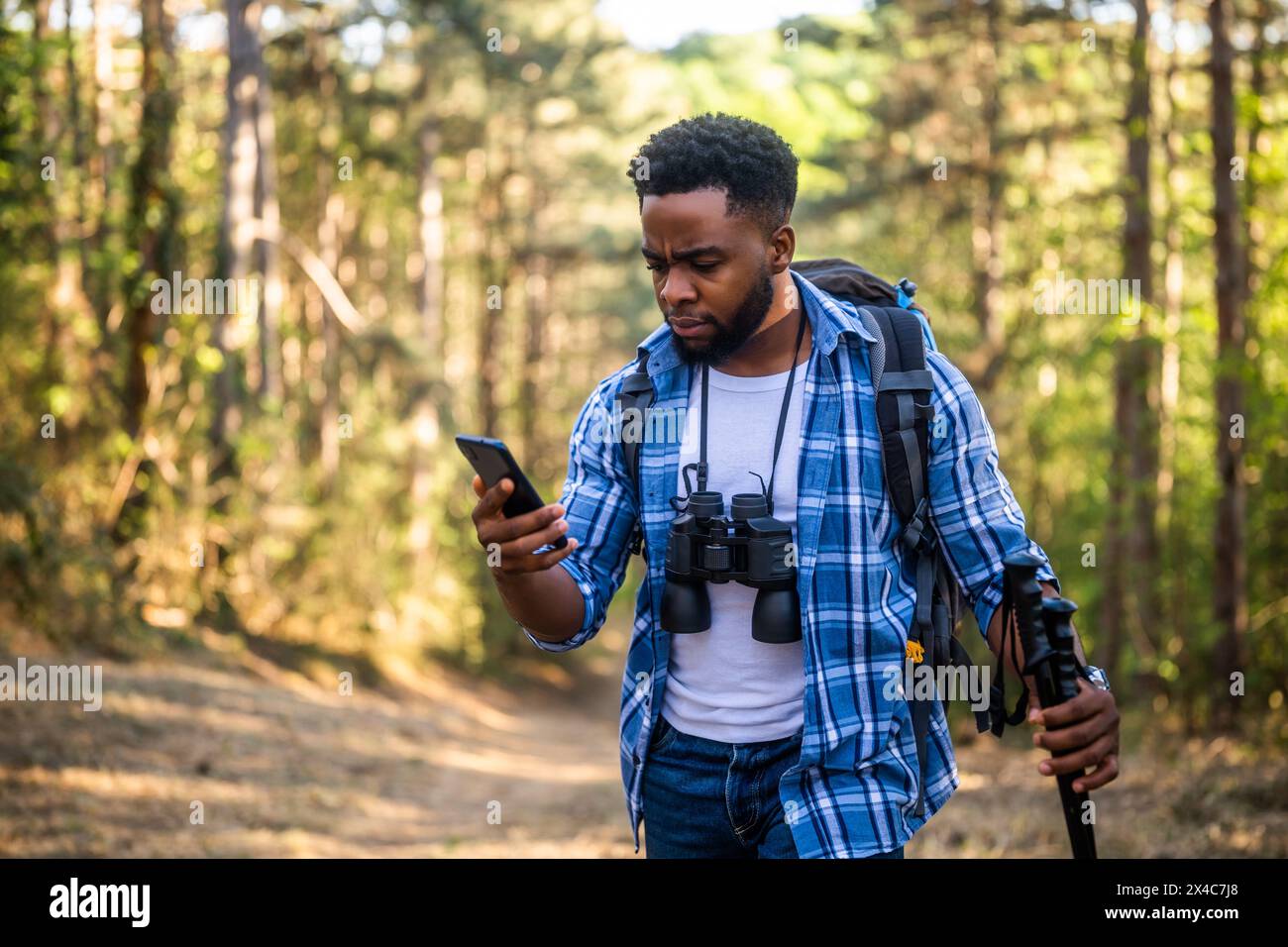 Ein besorgter Wanderer hat sich verirrt und er benutzt ein Telefon, um die richtige Richtung zu finden, während er in der Natur wandert. Stockfoto