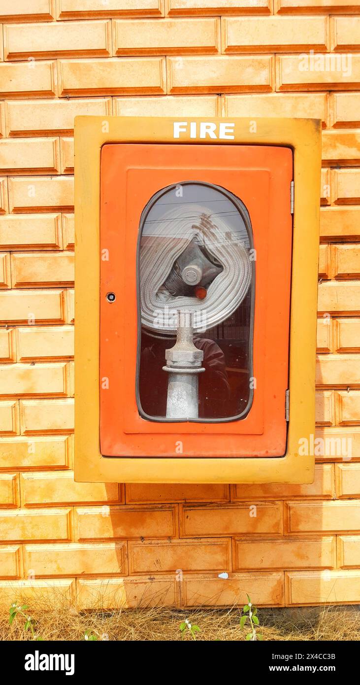 Notfeuerlöschschlauch in einem Kasten mit Glasfront, der an einer Wand befestigt ist, die an einem Metallhydranten befestigt ist, um im Notfall Wasserdurchfluss und -Druck bereitzustellen. Stockfoto