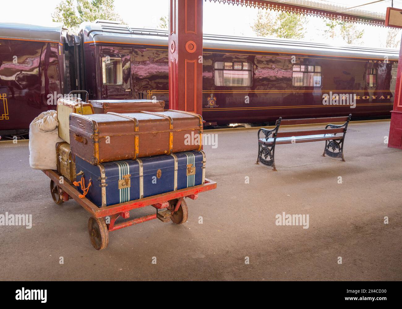 Alte Koffer auf einem Gepäckanhänger am Bahnhof Aviemore mit dem Royal Scotsman Zug zur Abfahrt bereit. Stockfoto