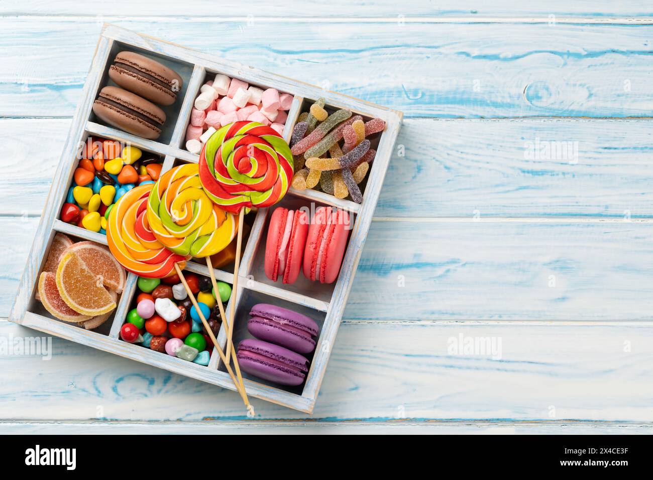 Verschiedene bunte Süßigkeiten, Lutscher und Makronen. Flach legen Süßigkeiten in der Box über hölzernem Hintergrund mit Kopierraum Stockfoto