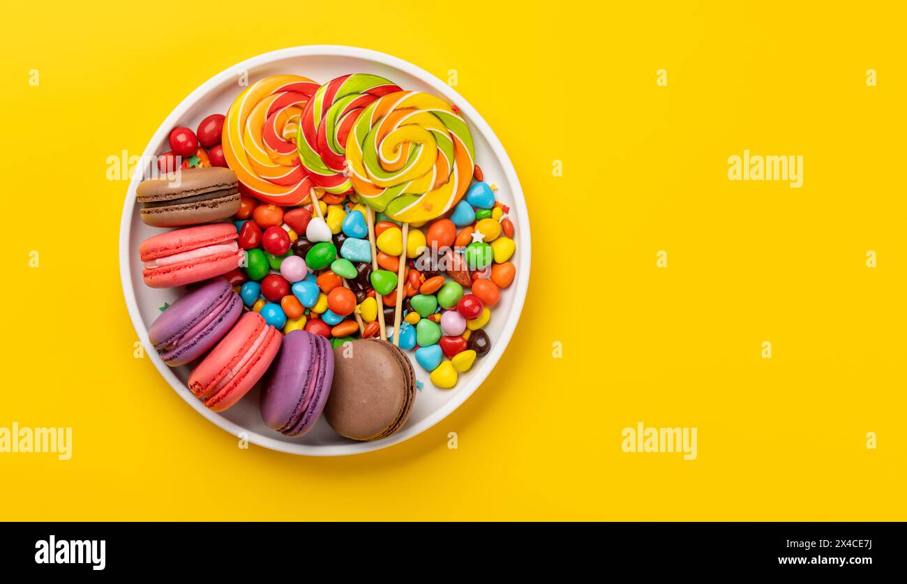 Verschiedene bunte Süßigkeiten, Lutscher und Makronen. Flach über gelbem Hintergrund mit Kopierraum Stockfoto