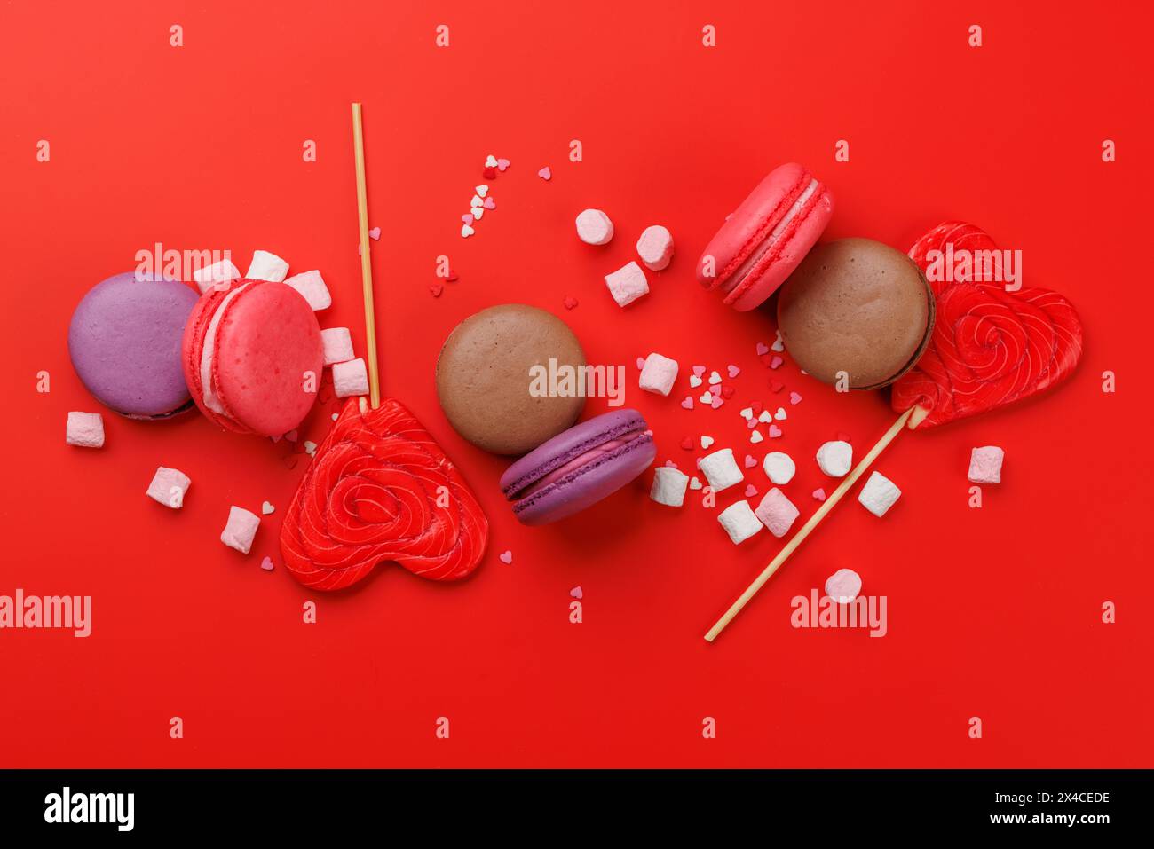 Verschiedene bunte Süßigkeiten, Lutscher und Makronen. Flach über rotem Hintergrund Stockfoto