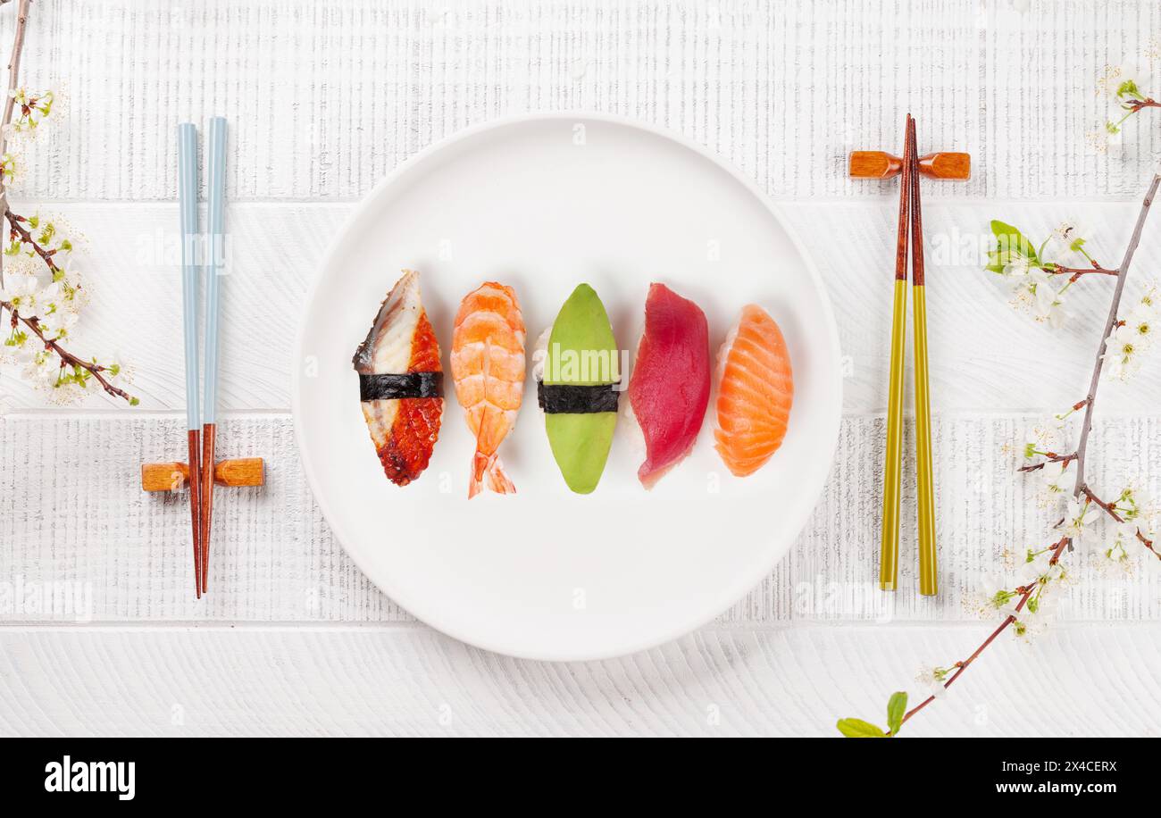 Sushi-Teller auf dem Tisch, geschmückt mit Kirschblütenzweig und Essstäbchen, verkörpert die japanische Esskultur Stockfoto