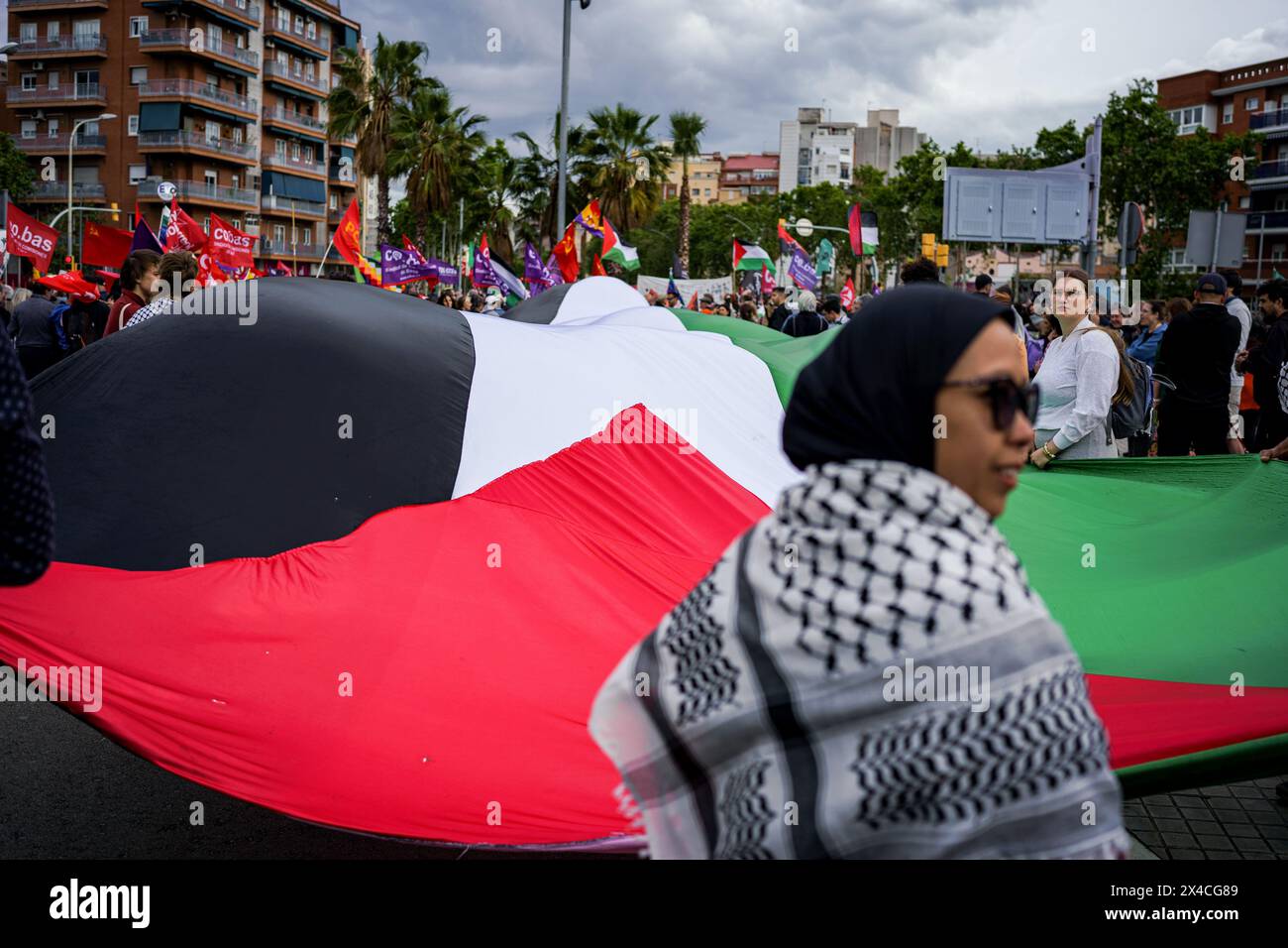 Barcelona, Spanien. Mai 2024. Eine Frau hält während der Demonstration eine riesige palästinensische Flagge. Tausende von Menschen marschierten in Barcelona und in den wichtigsten Städten Spaniens und forderten am Internationalen Arbeitstag bessere Löhne und Arbeitsbedingungen. Quelle: SOPA Images Limited/Alamy Live News Stockfoto