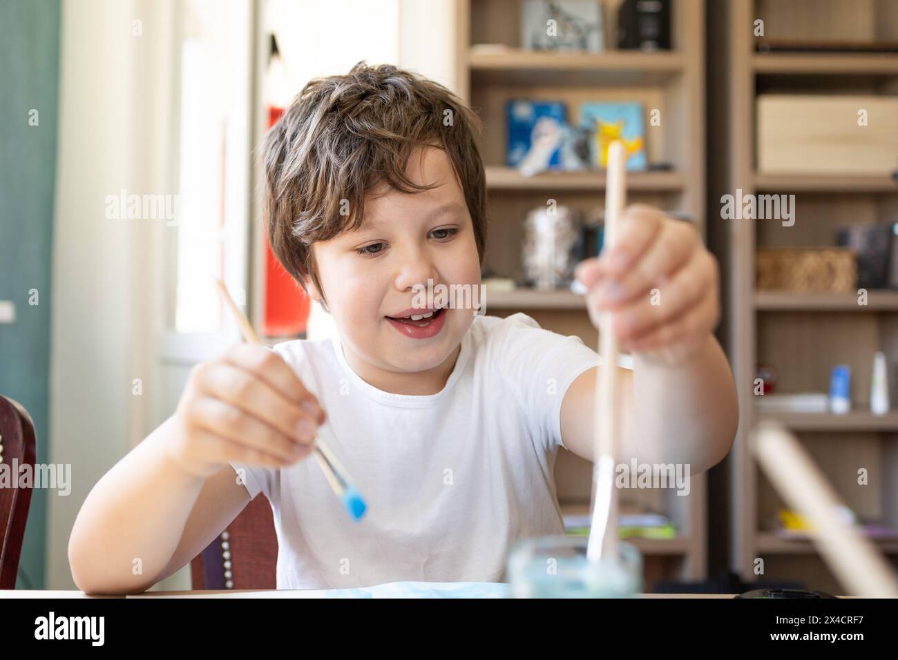 Ein kleiner Junge sitzt an seinem hölzernen Schreibtisch, umgeben von einer Vielzahl von lebhaften Aquarellfarben. Stockfoto