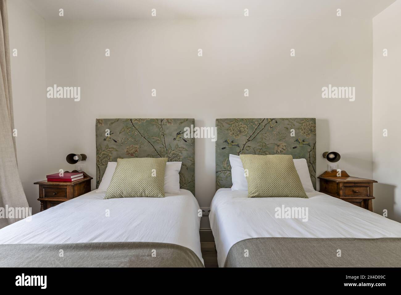 Ein Schlafzimmer mit Twin-Betten, Kopfteilen mit bedrucktem Stoff, n Kissen und Kissen und hölzernen Beistelltischen im Vintage-Stil Stockfoto