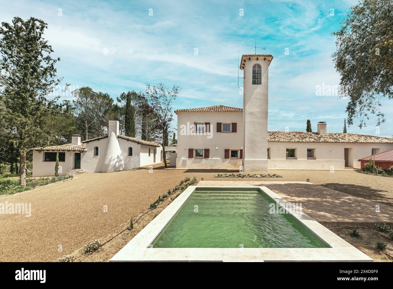 Ein Landhaus im andalusischen Stil, umgeben von grünen Bäumen und mit einem Pool aus grünen Fliesen Stockfoto