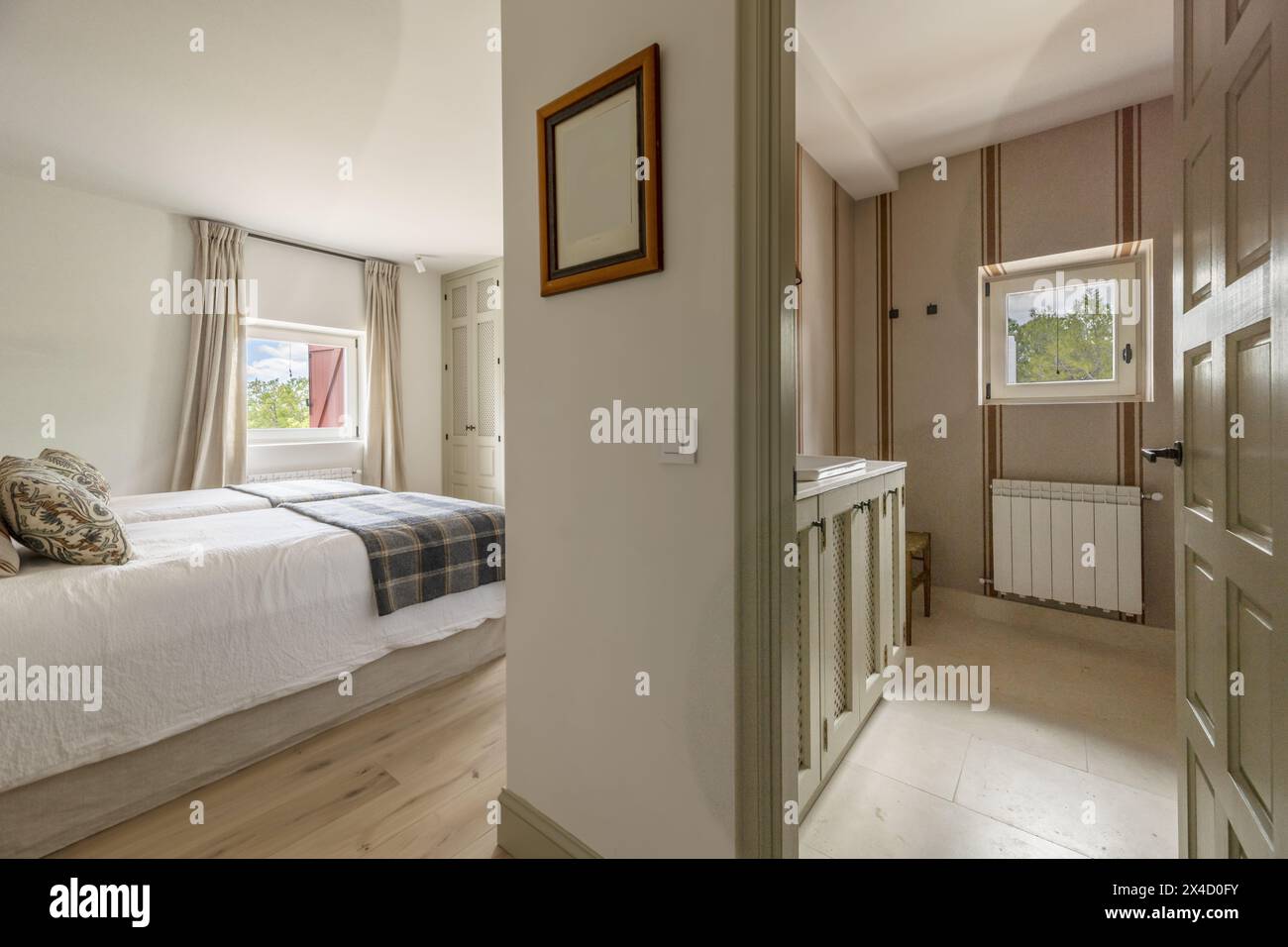Ein Schlafzimmer mit zusammengeschobenen Twin-Betten, Decken und Stoffpolsterkissen und einem Badezimmer im selben Zimmer Stockfoto