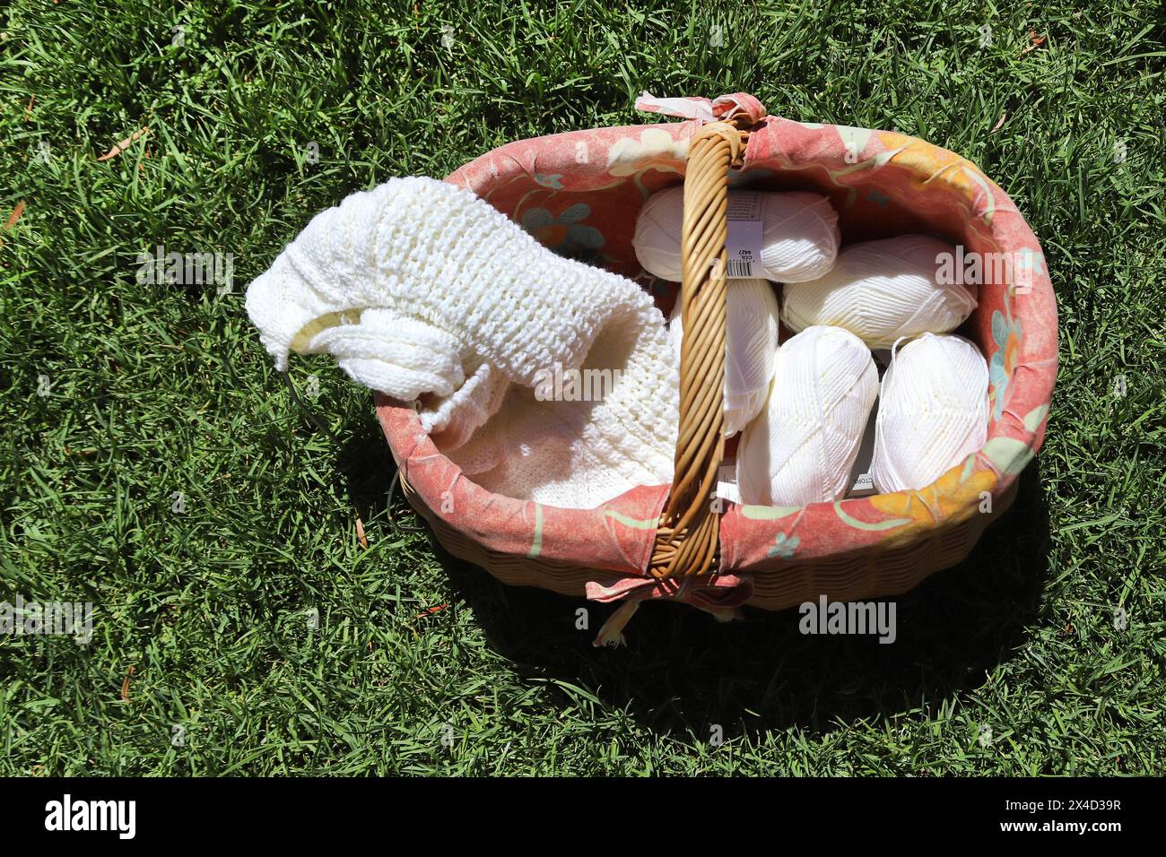 Strickkorb, Stricknadeln und weißes Garn zum Stricken, vor dem Hintergrund von grünem Gras, Stillleben Stockfoto