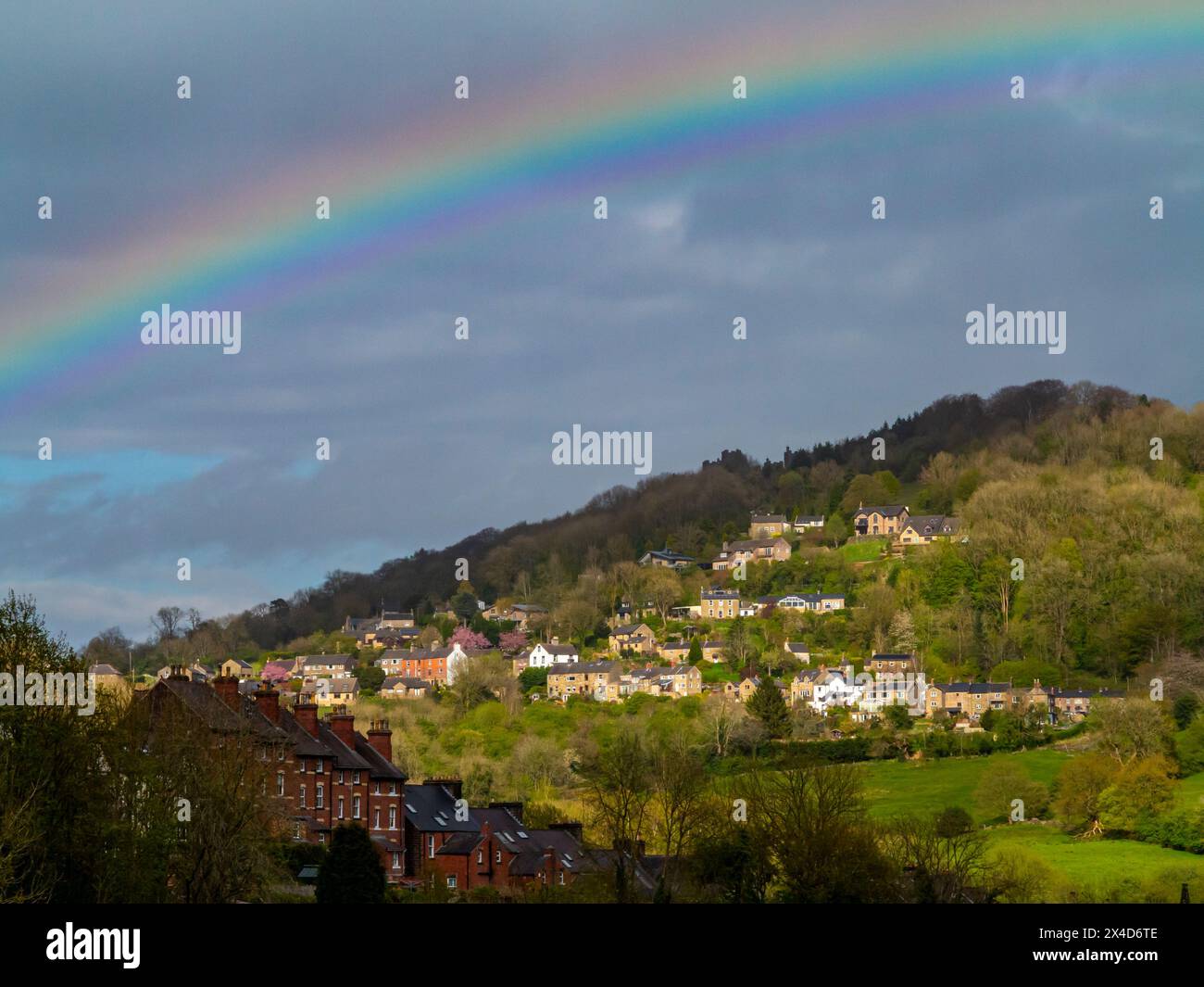 Regenbogen und stürmischer Himmel über dem Dorf Matlock Bath im Derbyshire Peak District England Großbritannien mit Starkholmes sichtbar auf dem Hügel dahinter. Stockfoto