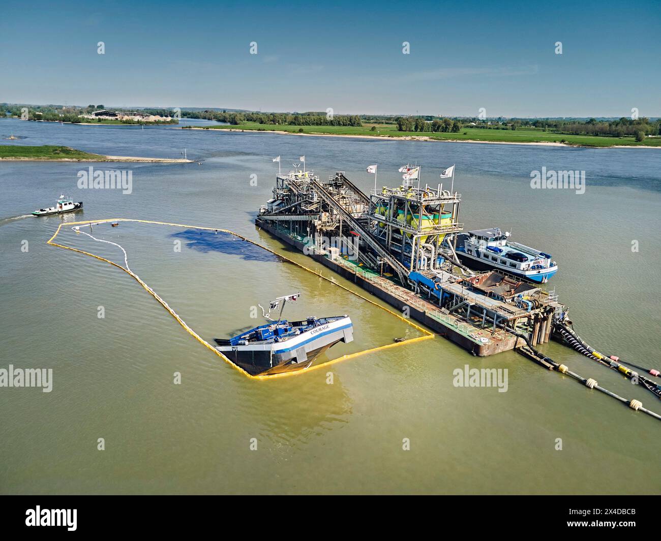 2. Mai 2024, Deest, Gelderland, Niederlande: (ANMERKUNG DER REDAKTION: Bild wird mit Drohne aufgenommen). Das Binnenschiff Courage (110 Meter lang und 50 Meter breit) brach am Mittwochmorgen beim Verladen von Sand auf einem Ausgrabungsgelände am Waal bei Deest in den Niederlanden. Austretendes Öl aus dem Behälter ist über dem Wasser sichtbar. Die niederländische Generaldirektion für öffentliche Arbeiten und Wasserwirtschaft (Rijkswaterstaat) hat Ölbooms eingeführt, um Verschmutzungen zu verhindern. Die Unfallursache ist noch unklar. (Credit Image: © Norbert Voskens/SOPA Images via ZUMA Press Wire) NUR REDAKTIONELLE VERWENDUNG! Nicht für Commer Stockfoto 2. Mai 2024, Deest, Gelderland, Niederlande: (ANMERKUNG DER REDAKTION: Bild wird mit Drohne aufgenommen). Das Binnenschiff Courage (110 Meter lang und 50 Meter breit) brach am Mittwochmorgen beim Verladen von Sand auf einem Ausgrabungsgelände am Waal bei Deest in den Niederlanden. Austretendes Öl aus dem Behälter ist über dem Wasser sichtbar. Die niederländische Generaldirektion für öffentliche Arbeiten und Wasserwirtschaft (Rijkswaterstaat) hat Ölbooms eingeführt, um Verschmutzungen zu verhindern. Die Unfallursache ist noch unklar. (Credit Image: © Norbert Voskens/SOPA Images via ZUMA Press Wire) NUR REDAKTIONELLE VERWENDUNG! Nicht für Commer Stockfoto