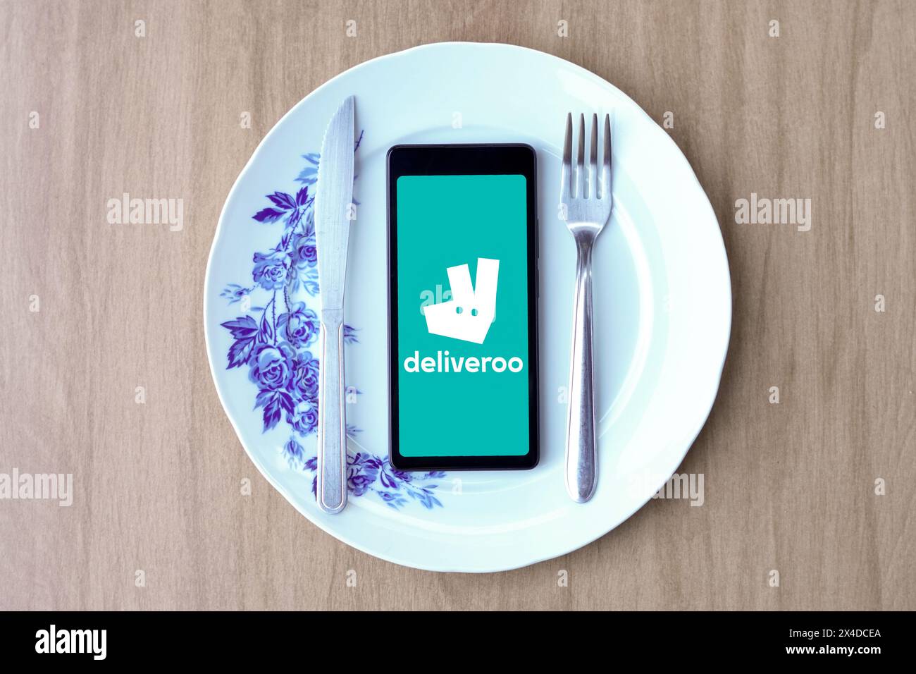 In dieser Fotoabbildung wird das Deliveroo Logo auf einem Smartphone-Bildschirm auf einem Teller mit Besteck angezeigt. Stockfoto