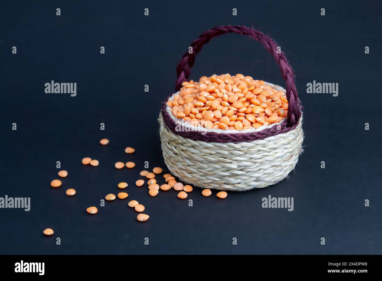 Rote Linsen stapeln sich isoliert. Trockene orangene Linsenkörner, Haufen von Dal, roh Daal, Dhal, Masoor, Lens culinaris oder Lens esculenta auf Jutekorb. Stockfoto