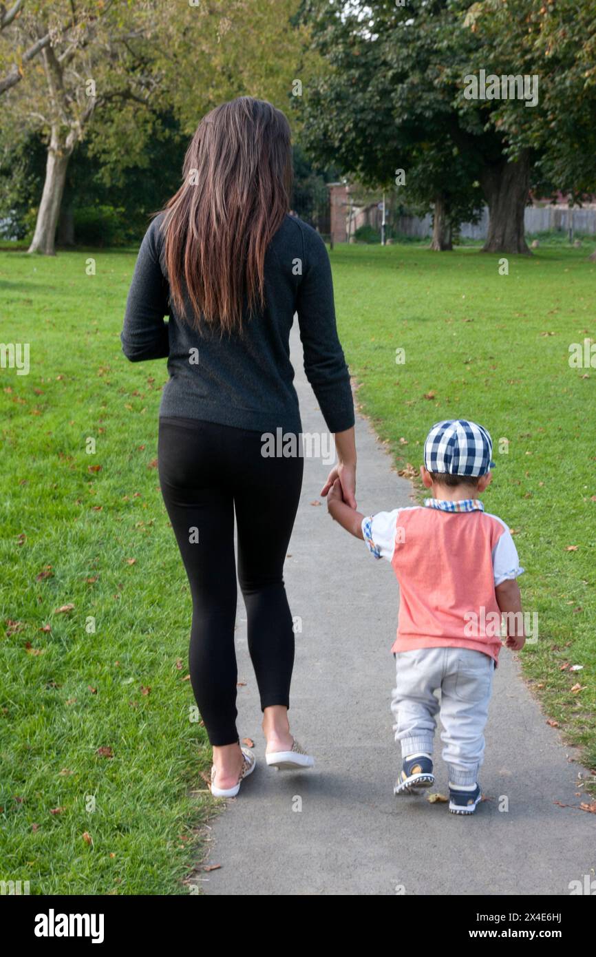 Eine junge Frau, die mit einem Kleinkind den Weg entlang geht Stockfoto