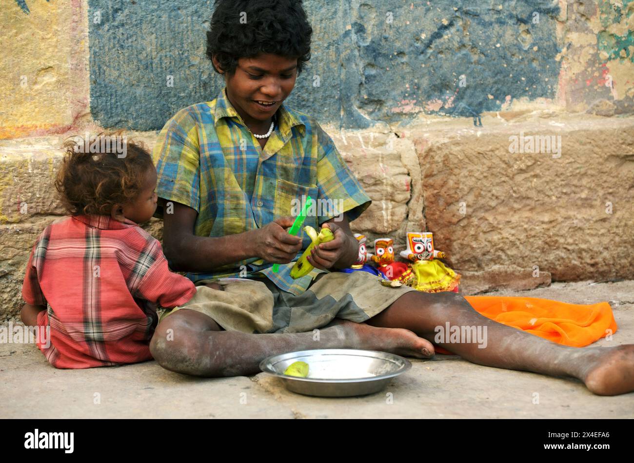 Junge und Kleinkind teilen sich eine Banane, während sie kleine Statuen in Varanasi, Indien, verkaufen Stockfoto