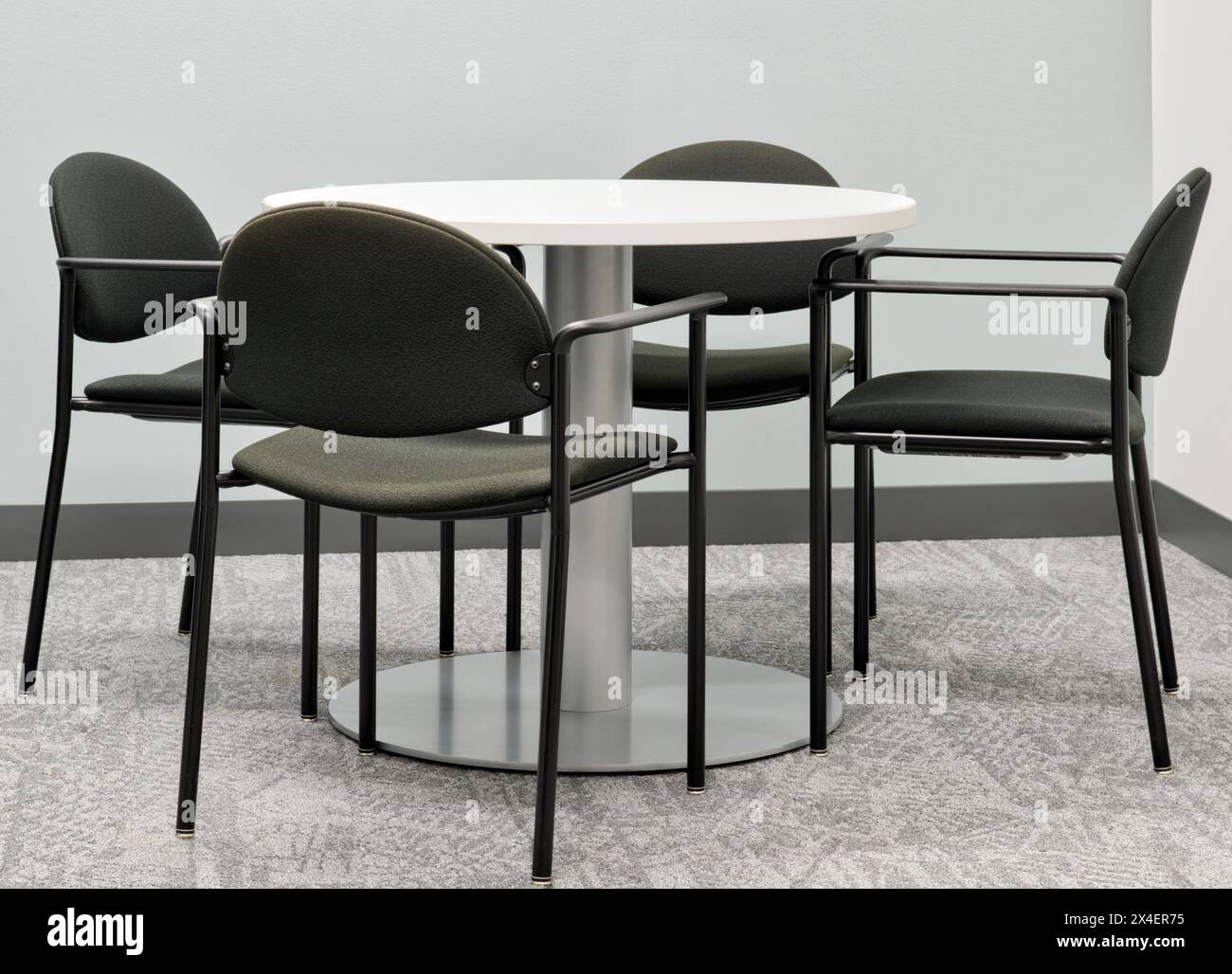 Runder Tisch, vier schwarze Stühle im Büro, grauer Teppich, keine Leute. Stockfoto