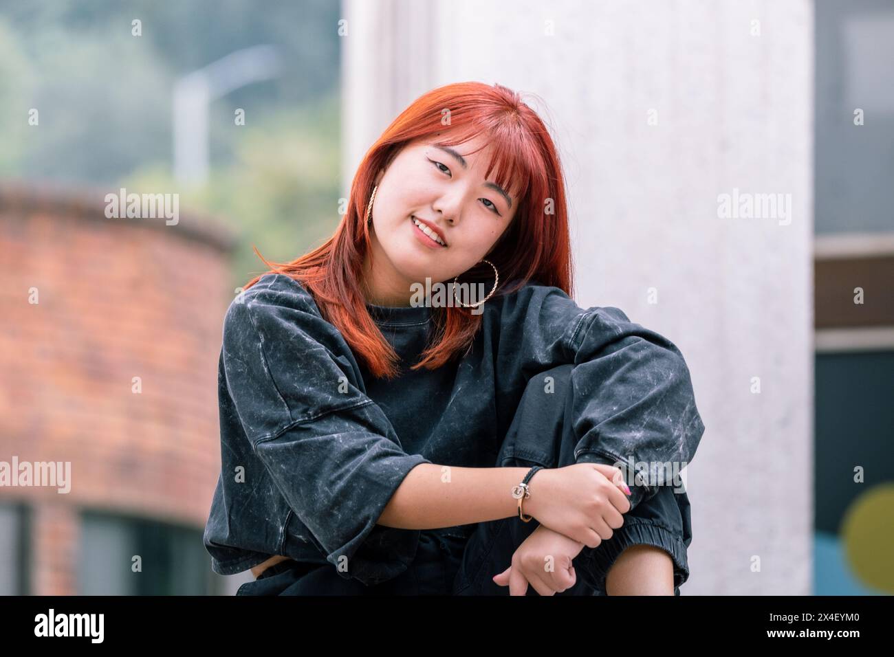 Koreanische Tänzerin mit roten Haaren genießt einen entspannten Moment während einer Outdoor-Pause Stockfoto