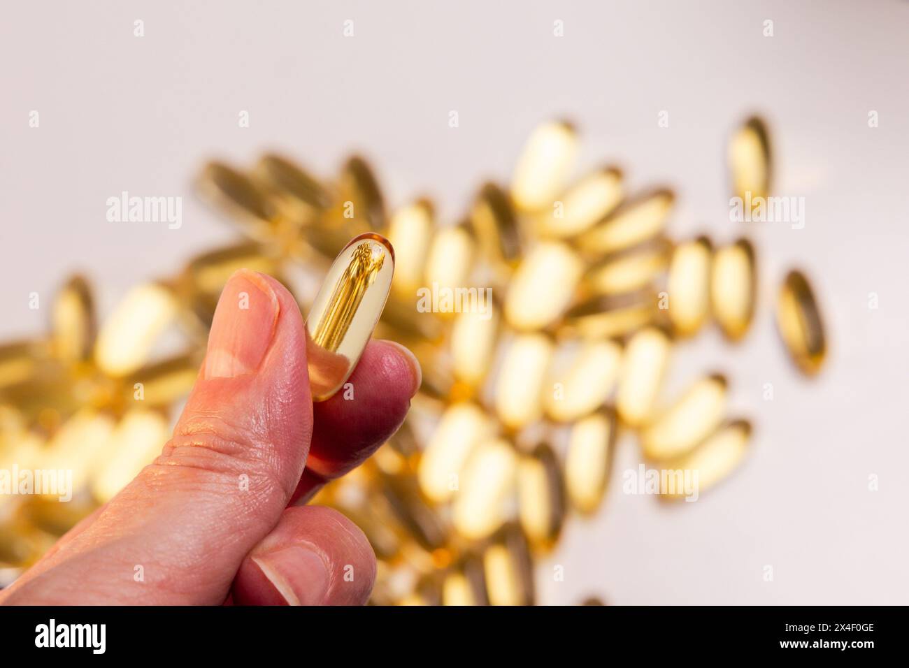 Die Hand der Frau hält eine Pille Fischöl mit Omega 3 mit einer goldgelben Farbe, einem essentiellen Nährstoff Stockfoto