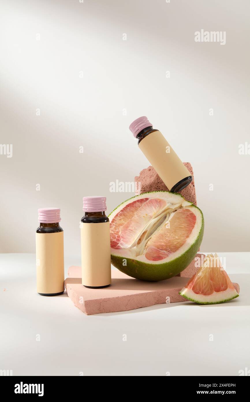 Szene für Werbung und Branding von Produkten mit Zutat aus Pomelo. Vorderansicht der Arzneimittelflaschen mit Pomelo-Scheiben auf rosa Ziegeln Stockfoto