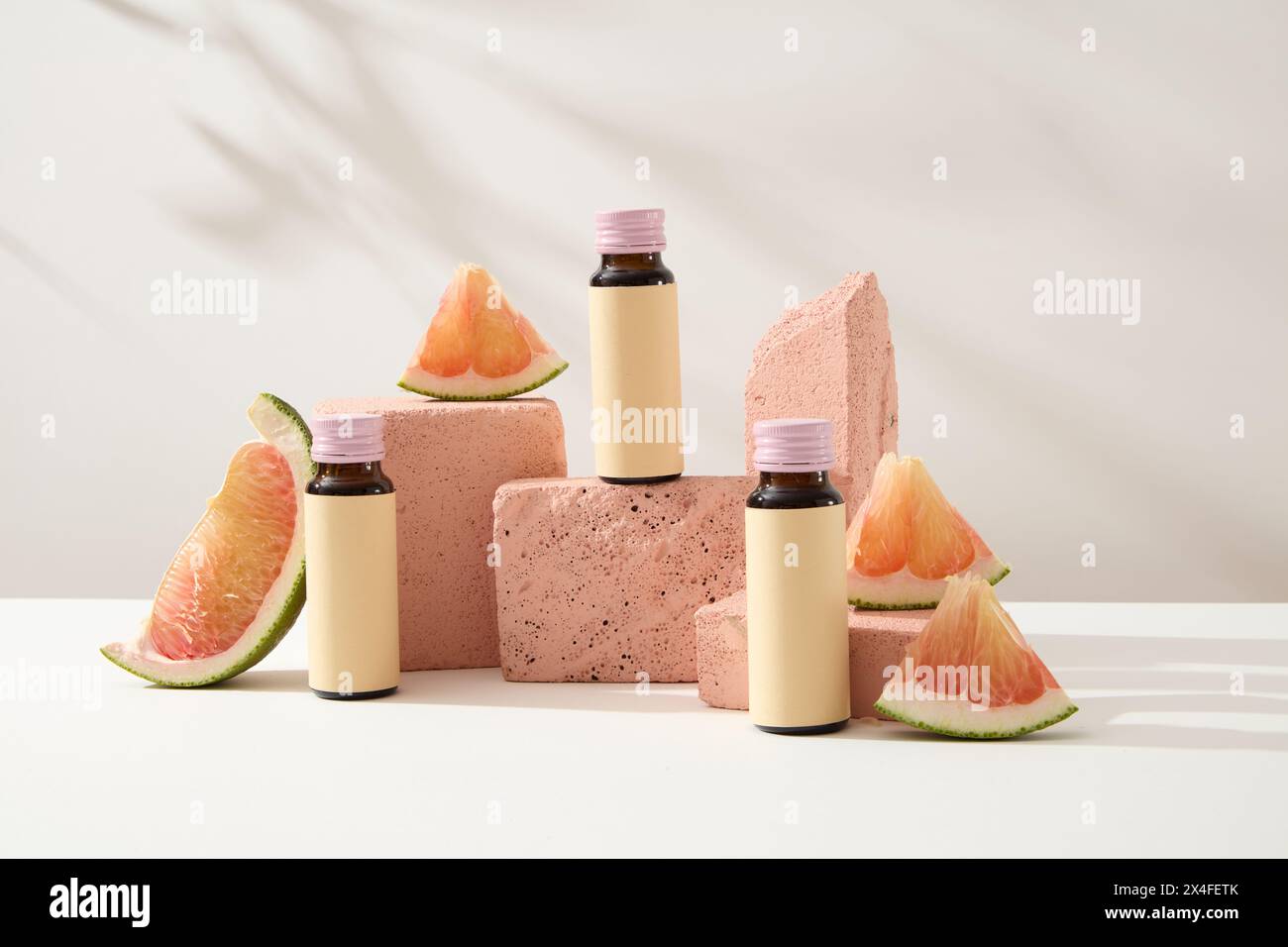 Minimaler Stil für die Produktpräsentation. Modell von Arzneiflaschen ohne Etikett, verziert mit Pomelo-Scheiben auf rosa Podesten auf weißem Hintergrund. Von Stockfoto