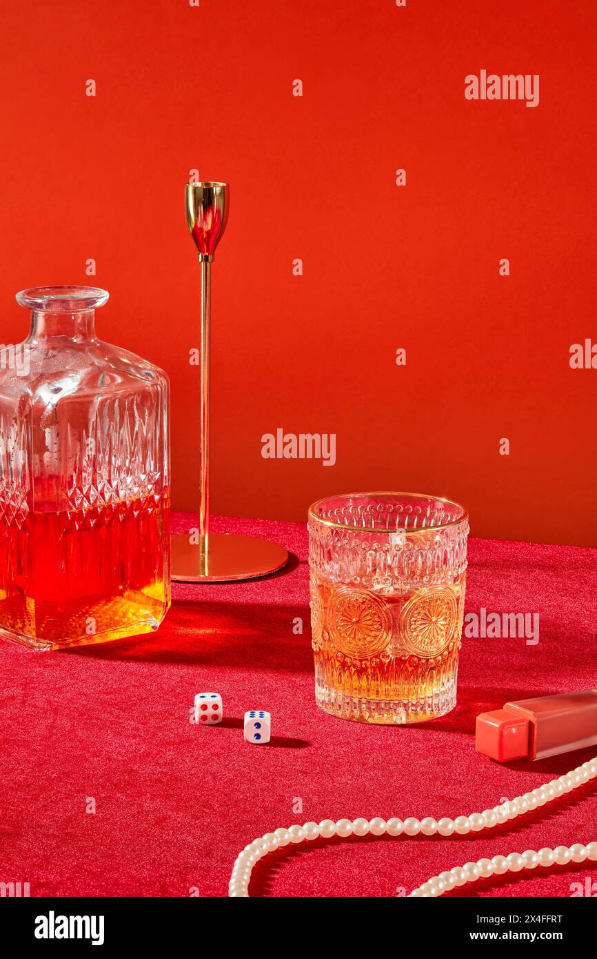 Glas leckeren Glühwein und Flasche mit Lippenstift und Perlenkette auf rotem Hintergrund. Vorderansicht, Werbefoto mit Leerraum f Stockfoto